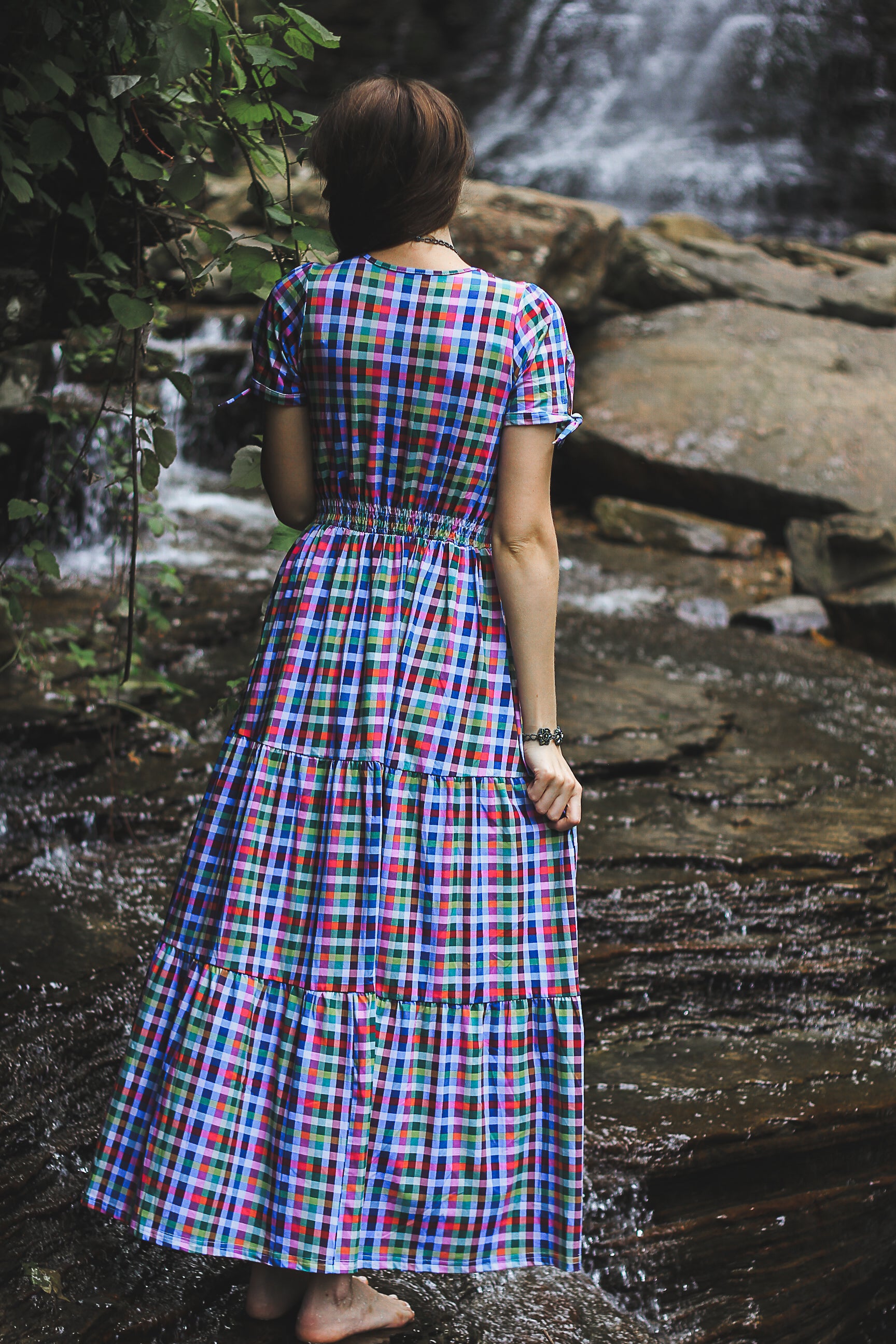 Woman in a colorful plaid modest nursing dress standing by a waterfall