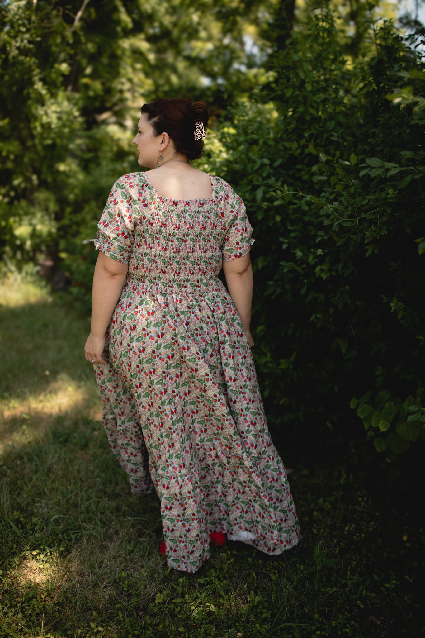 Woman in a floral modest nursing dress standing in a grassy area with trees