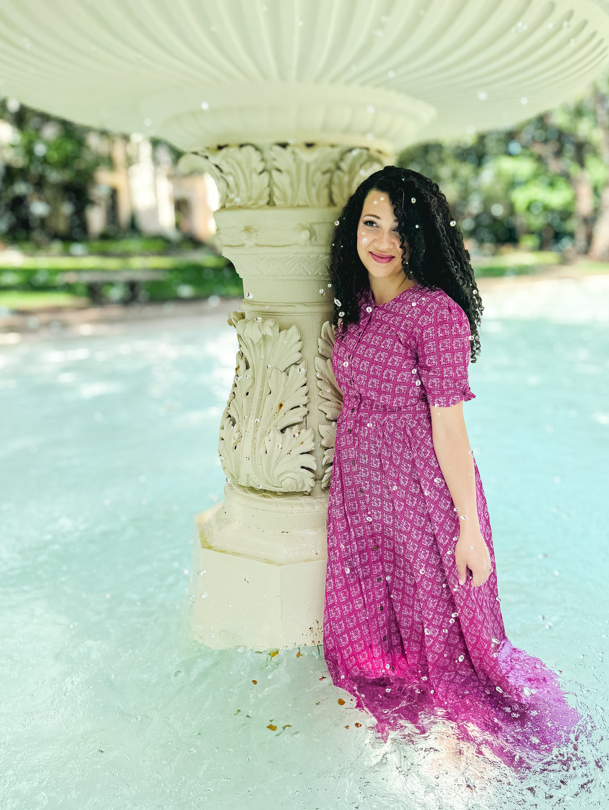 Woman in a pink modest nursing dress standing next to a fountain in a park