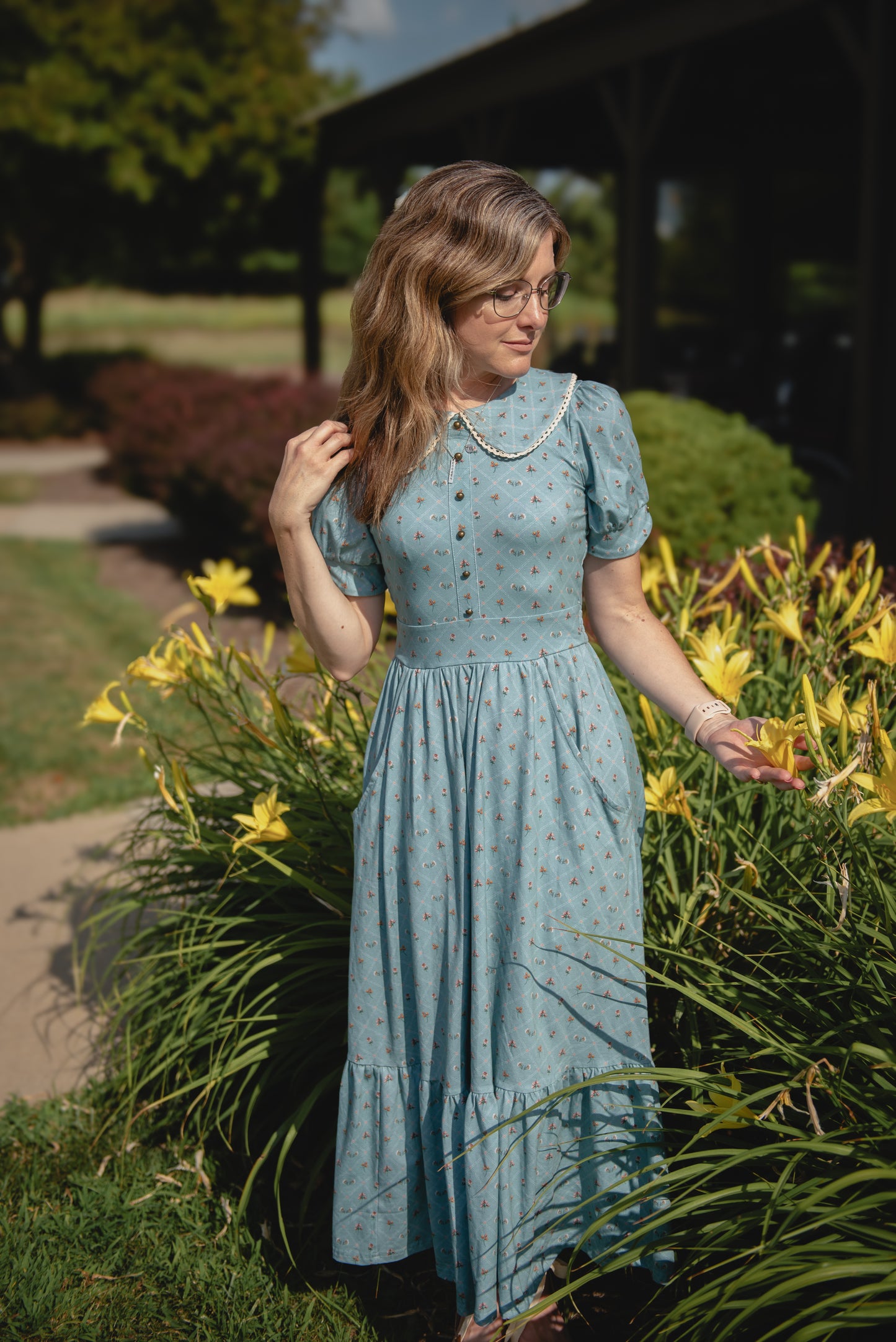 Woman in a light modest nursing dress standing in a garden with yellow flowers