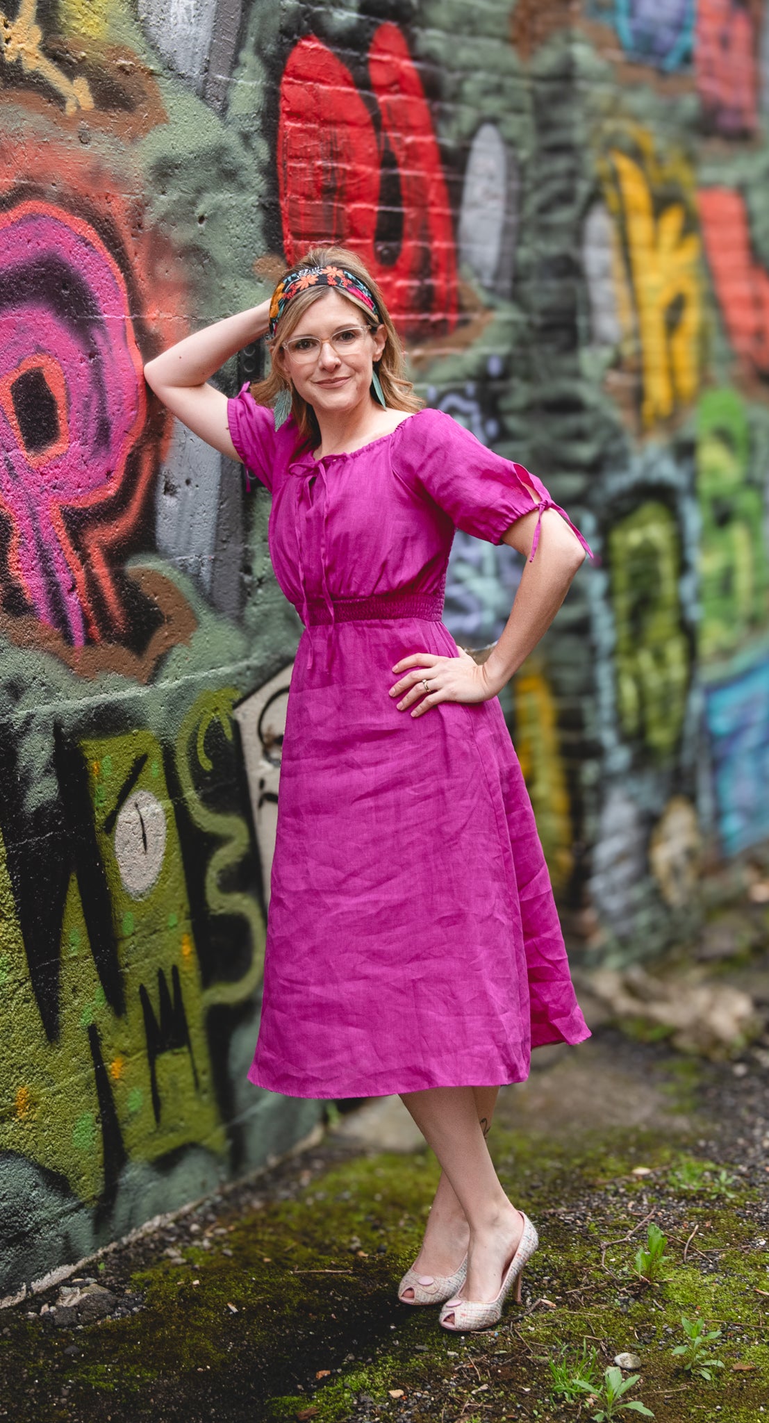 Woman in a pink modest nursing dress standing in front of a graffiti-covered wall