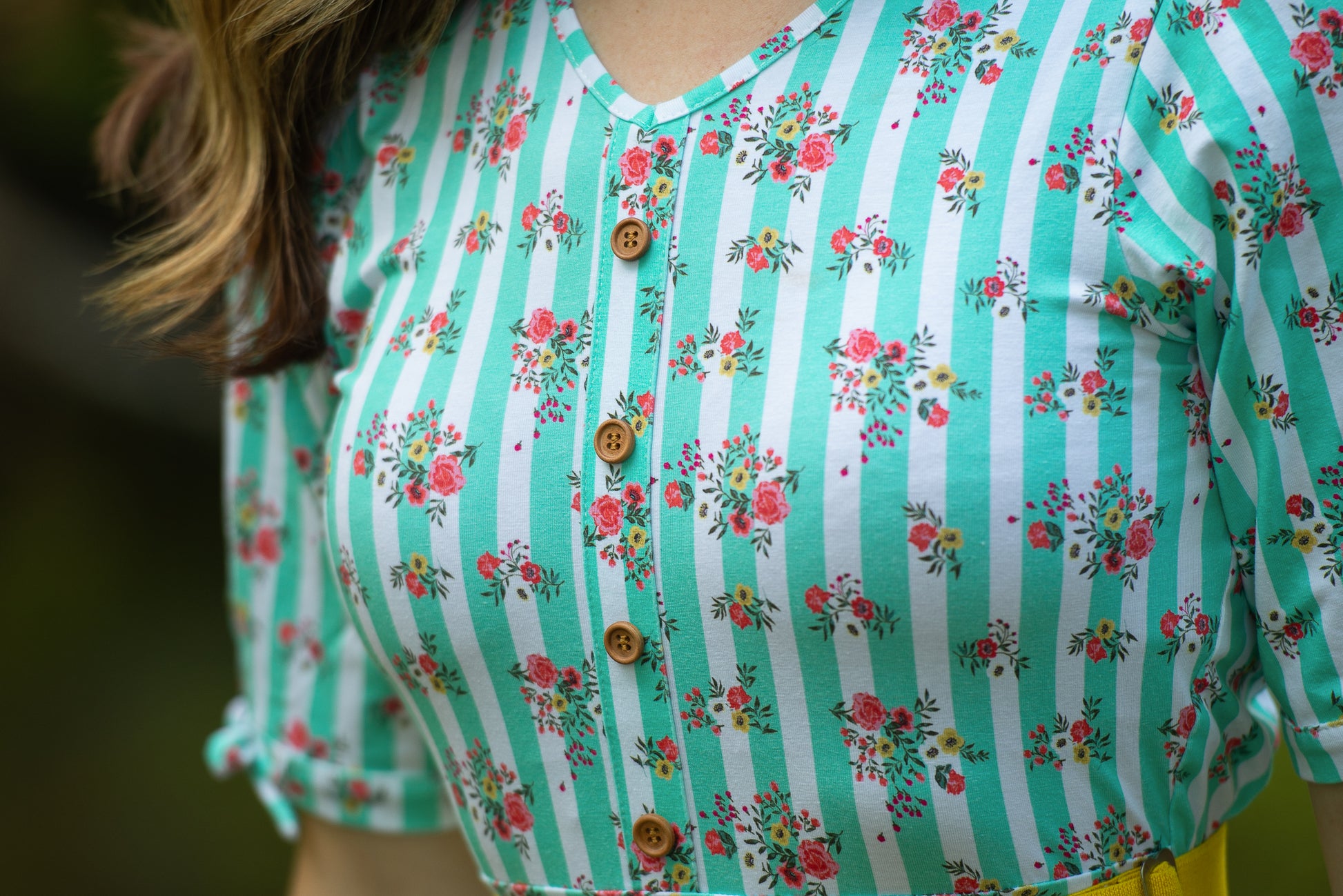 Close-up of a person wearing a green and white striped modest nursing dress with floral patterns.