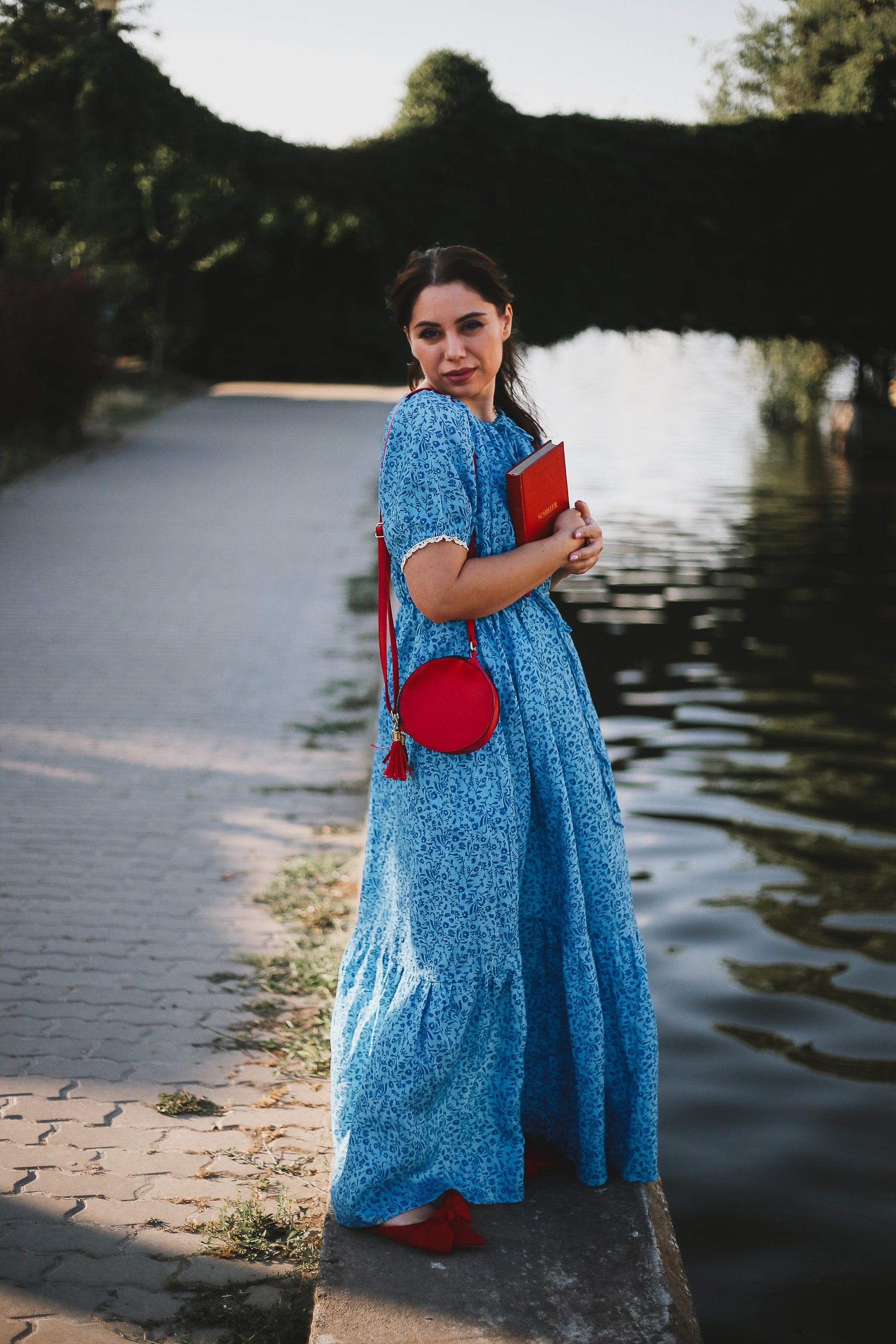 Woman in a blue modest nursing dress holding a red bag by a canal