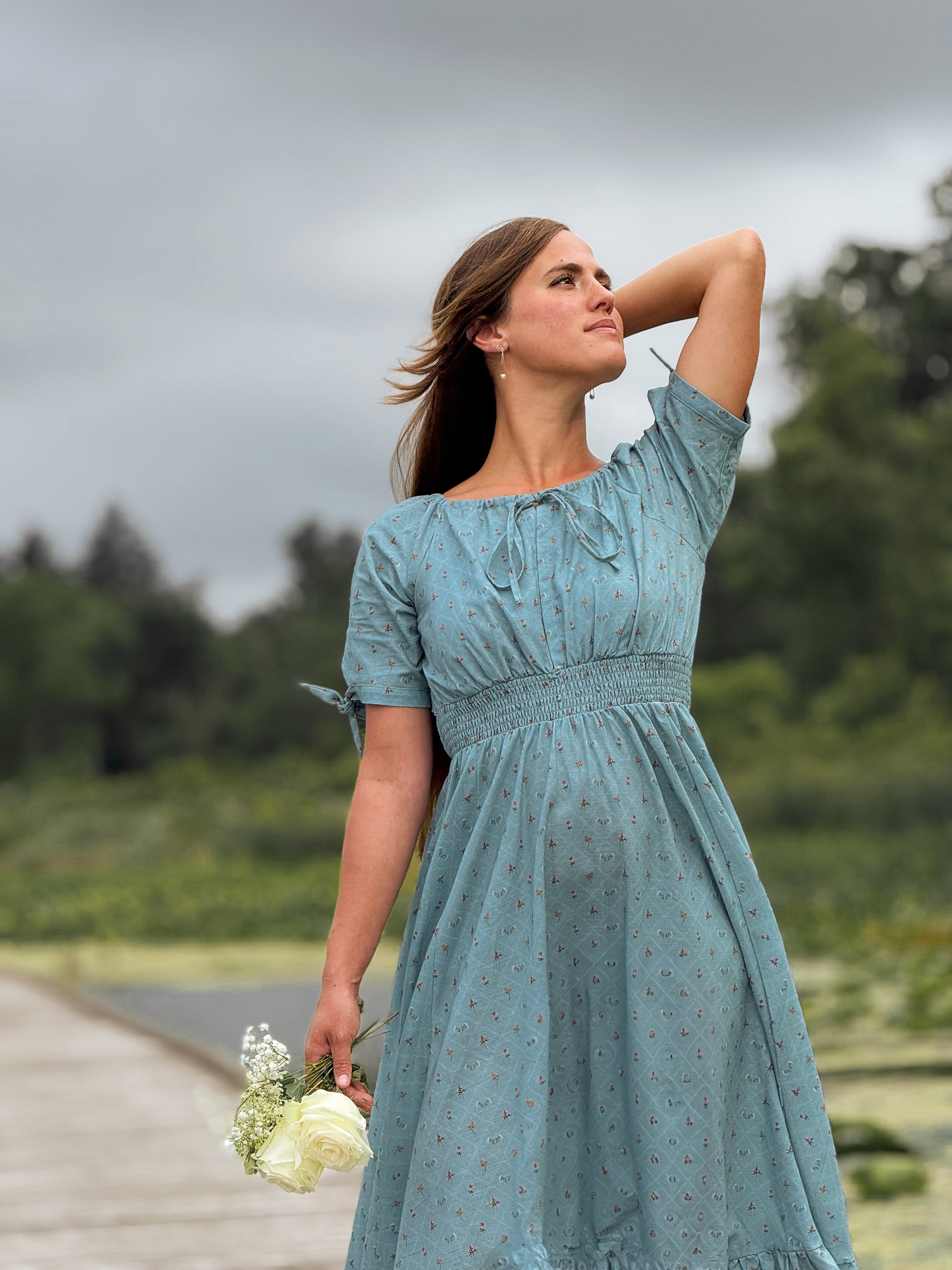 Woman in a blue modest nursing dress standing outdoors with trees in the background