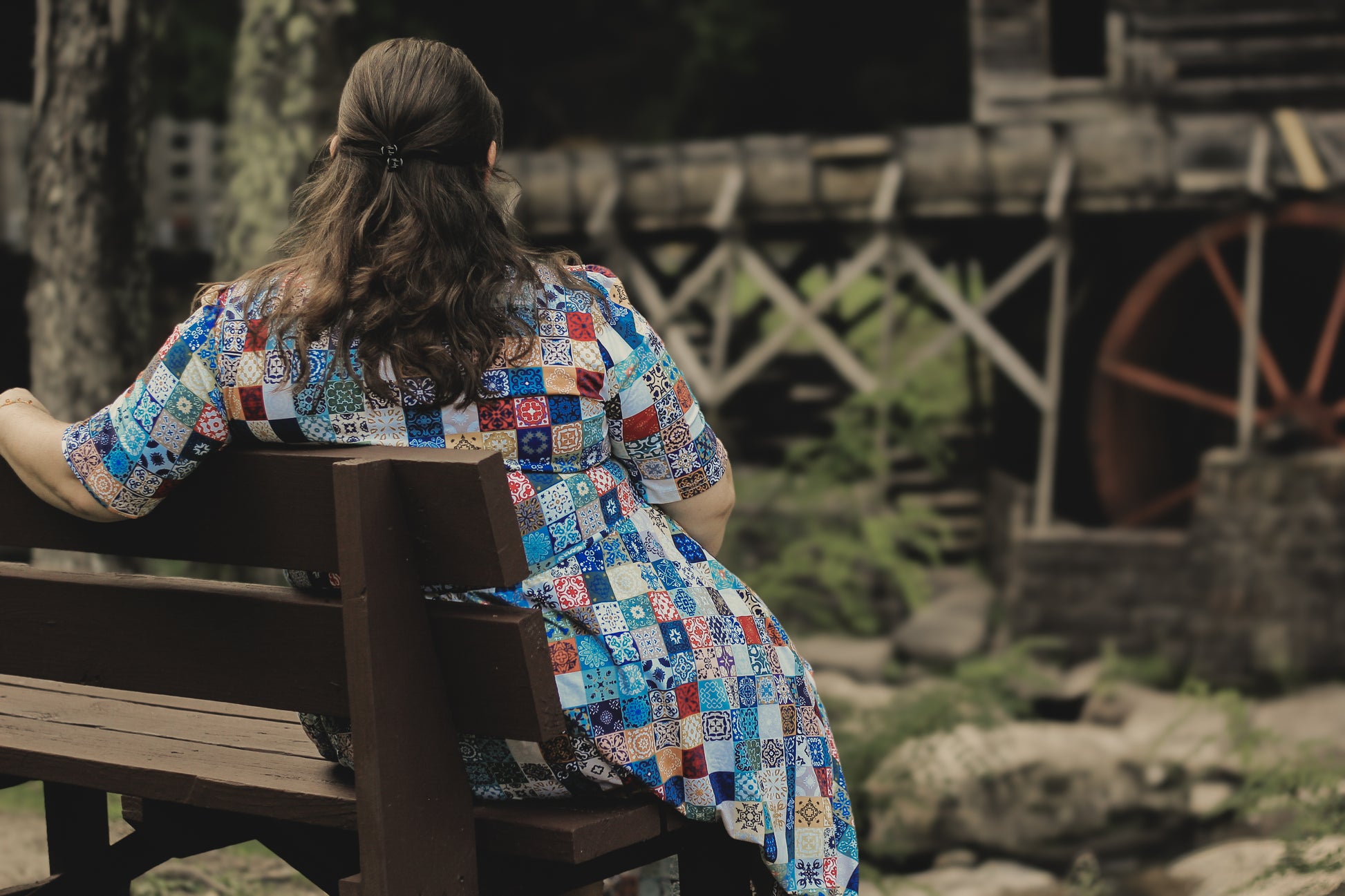 Woman in a colorful modest nursing dress sitting on a bench with a rustic background