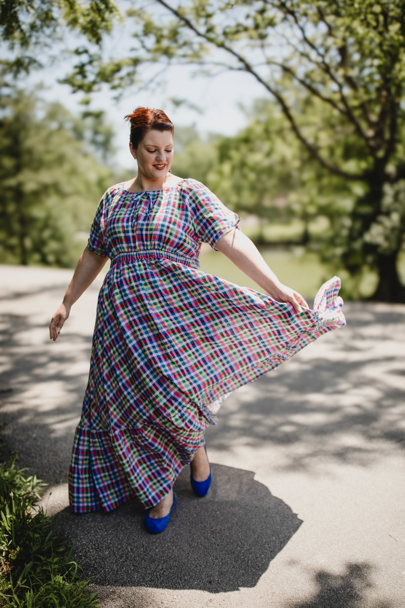 Woman in a colorful plaid modest nursing dress standing outdoors with trees in the background