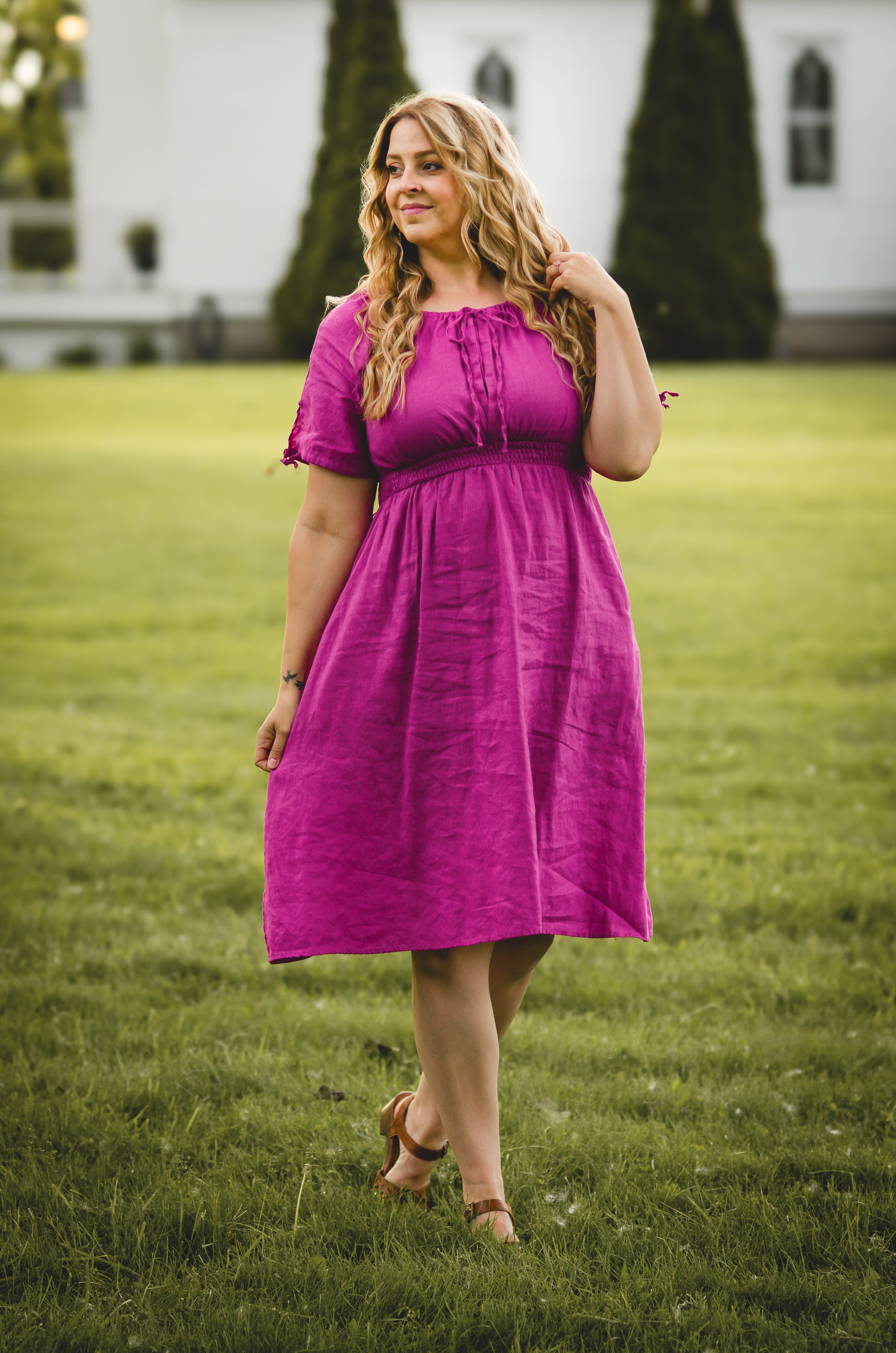 Woman in a pink modest nursing dress standing on grass with a white building in the background
