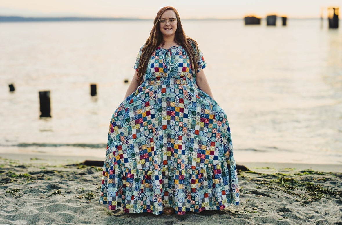 Woman in a colorful modest nursing dress standing on a beach with a blurred background