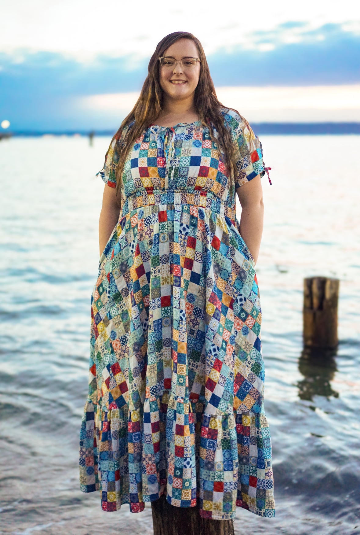 Woman wearing a colorful patterned modest nursing dress standing by a body of water.