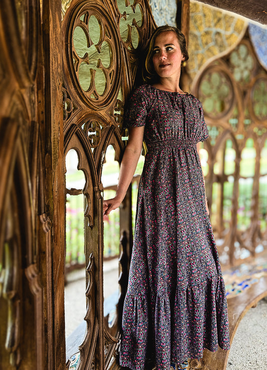 Woman in a floral modest nursing dress standing next to an ornate wooden door with stained glass windows in the background.