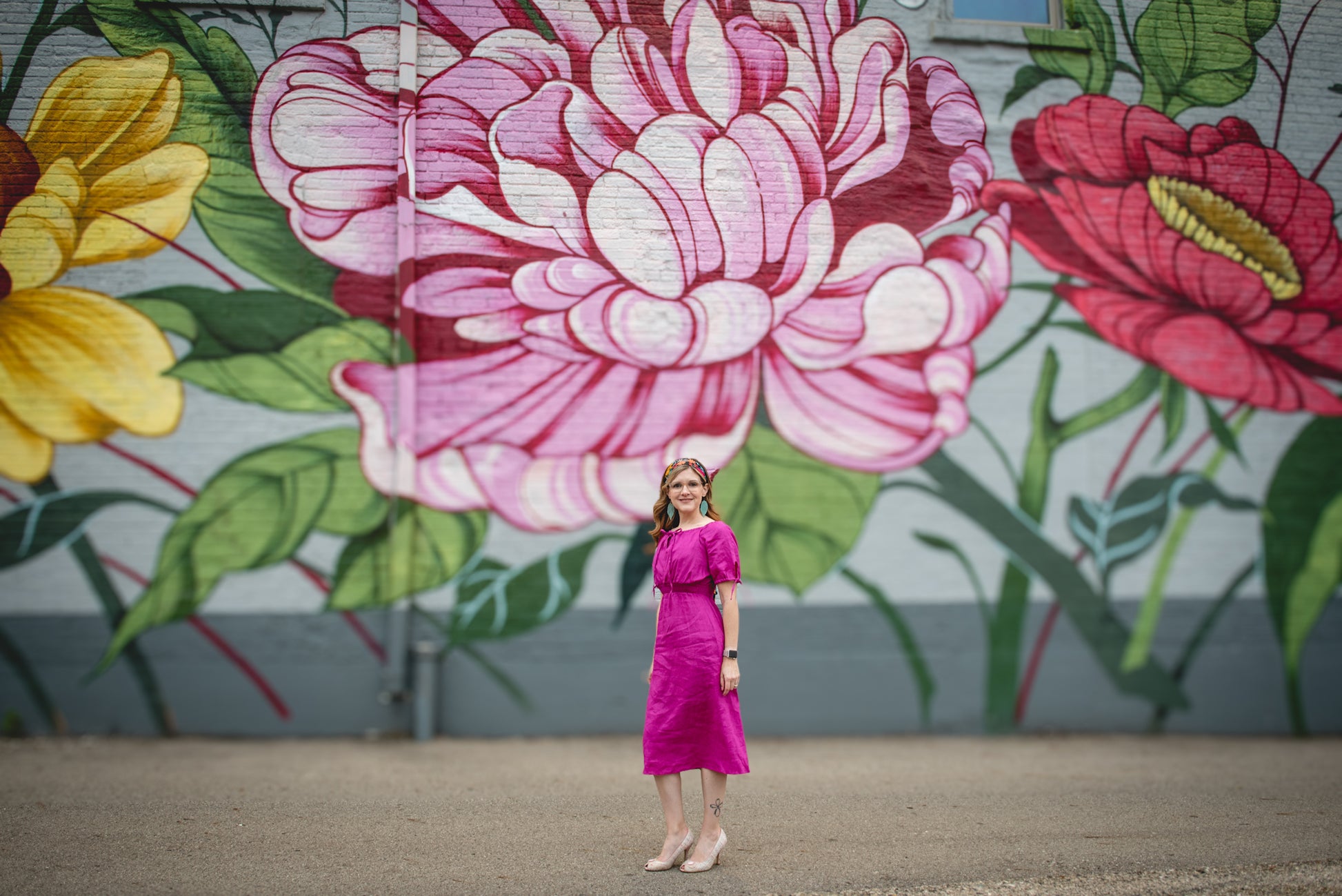 Woman in a pink modest nursing dress standing in front of a colorful floral mural.