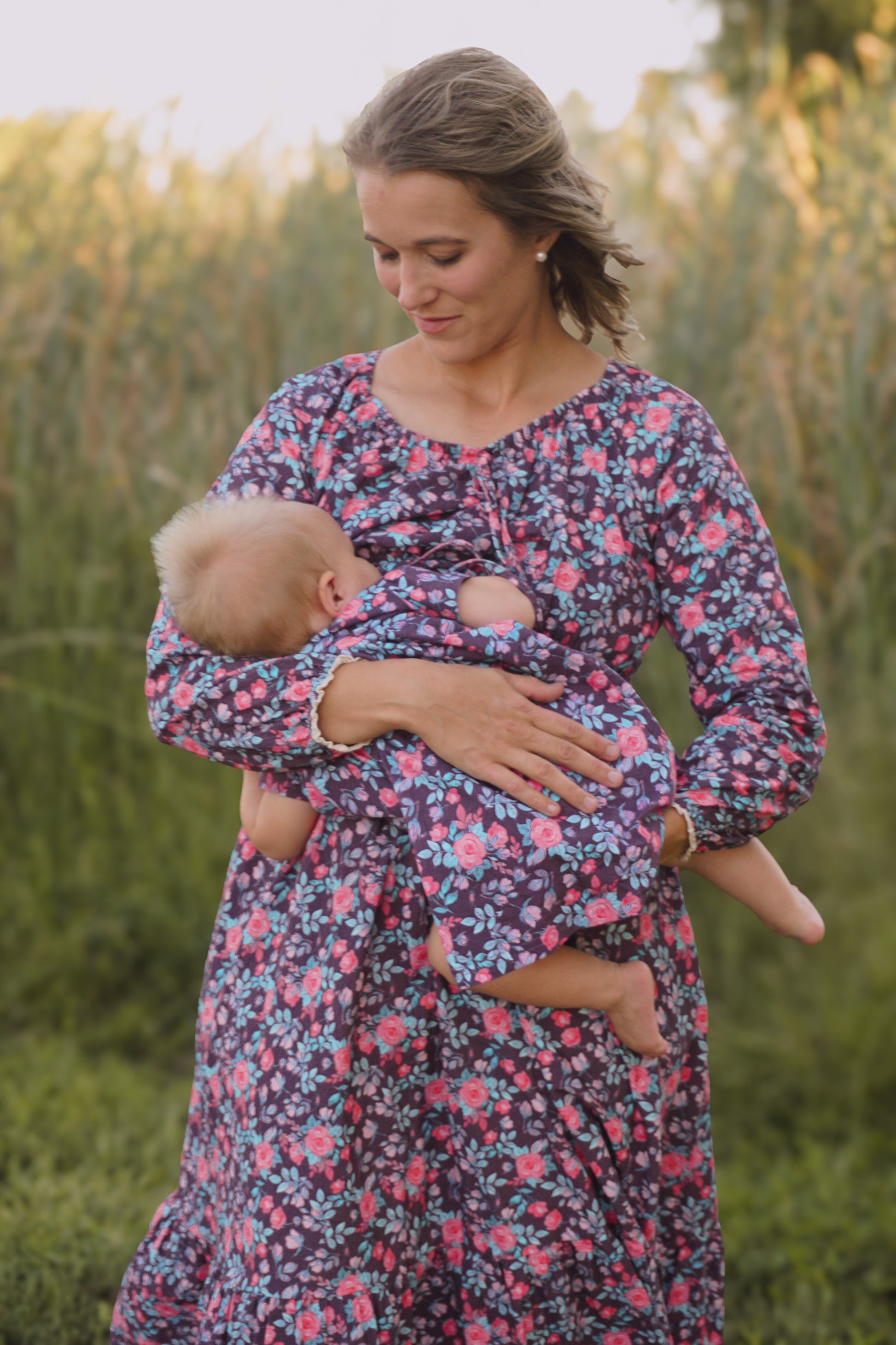 Woman in modest nursing floral dress holding baby in field