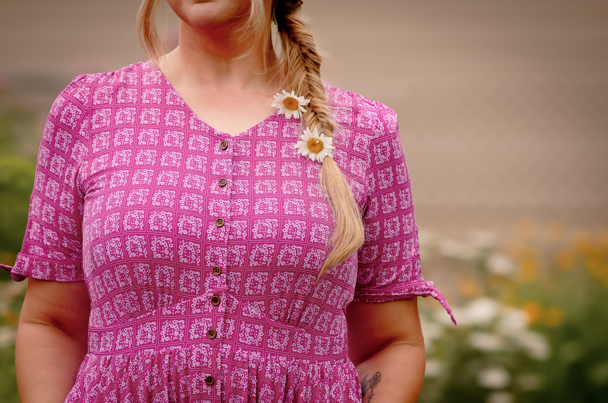 Woman wearing a pink patterned modest nursing dress with flowers in her hair, standing outdoors.