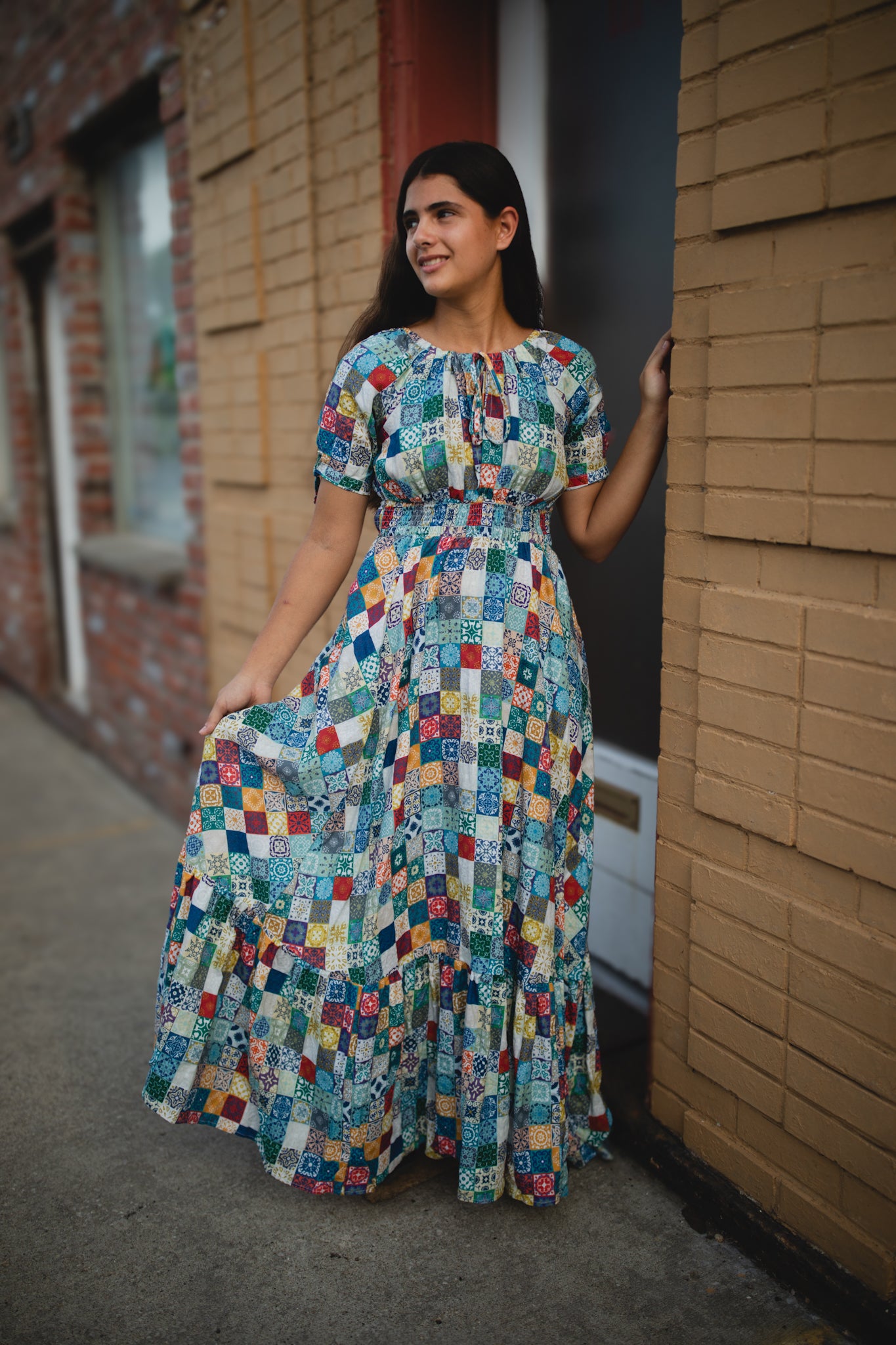 Woman wearing a colorful patterned modest nursing dress standing against a brick wall.