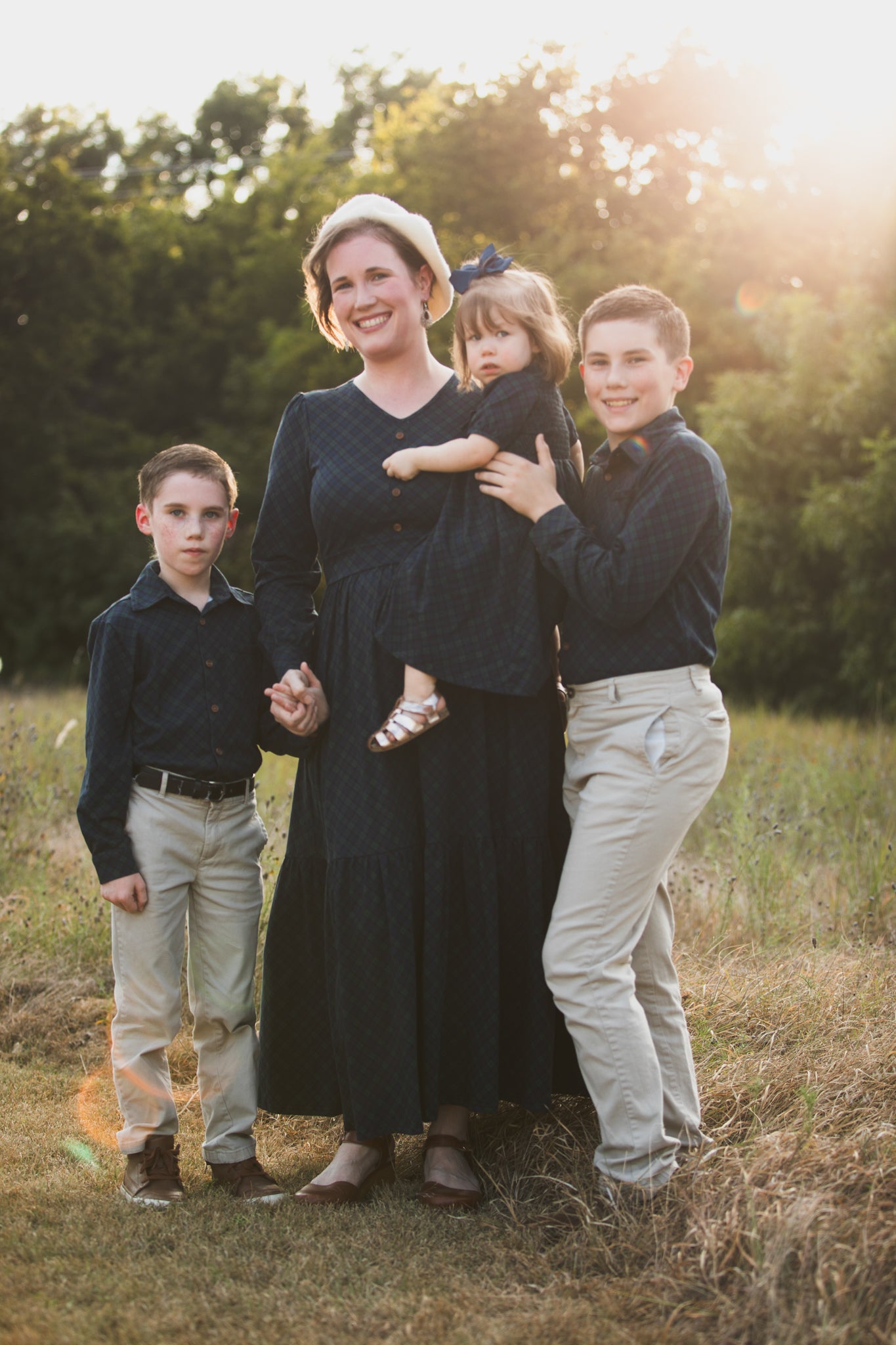 Mother in modest nursing dress with children in field at sunset