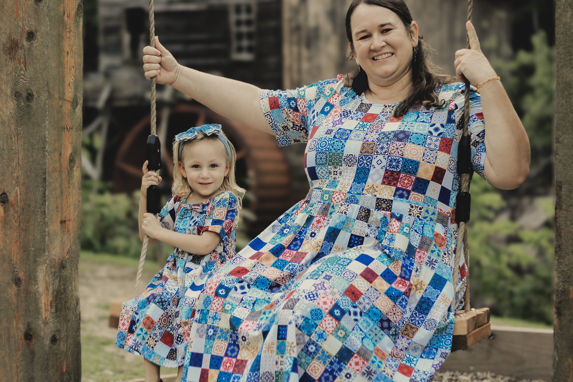 Woman and child in colorful patchwork modest dresses on a swing set.