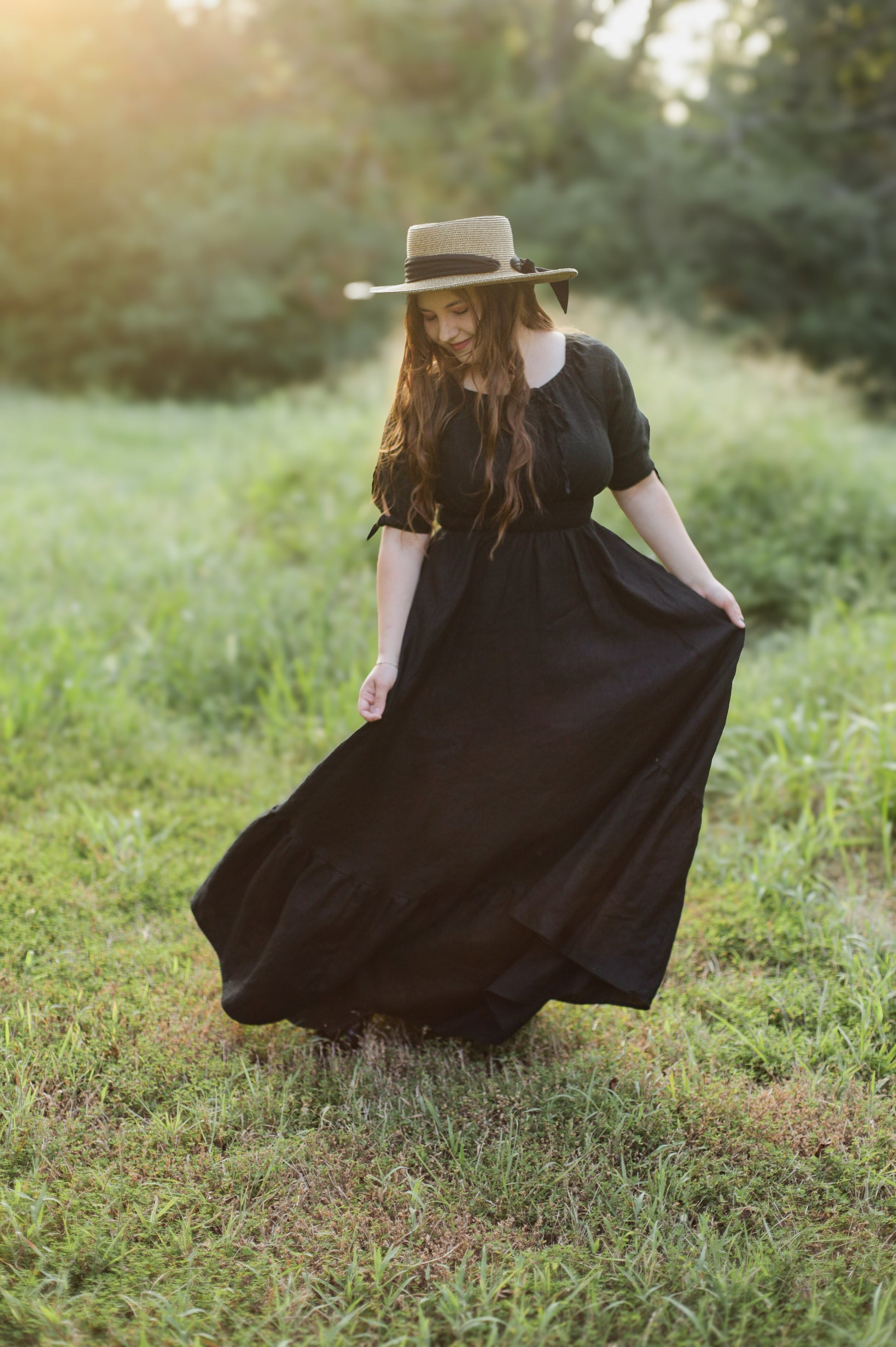 Woman in a black modest nursing dress and hat standing in a grassy field