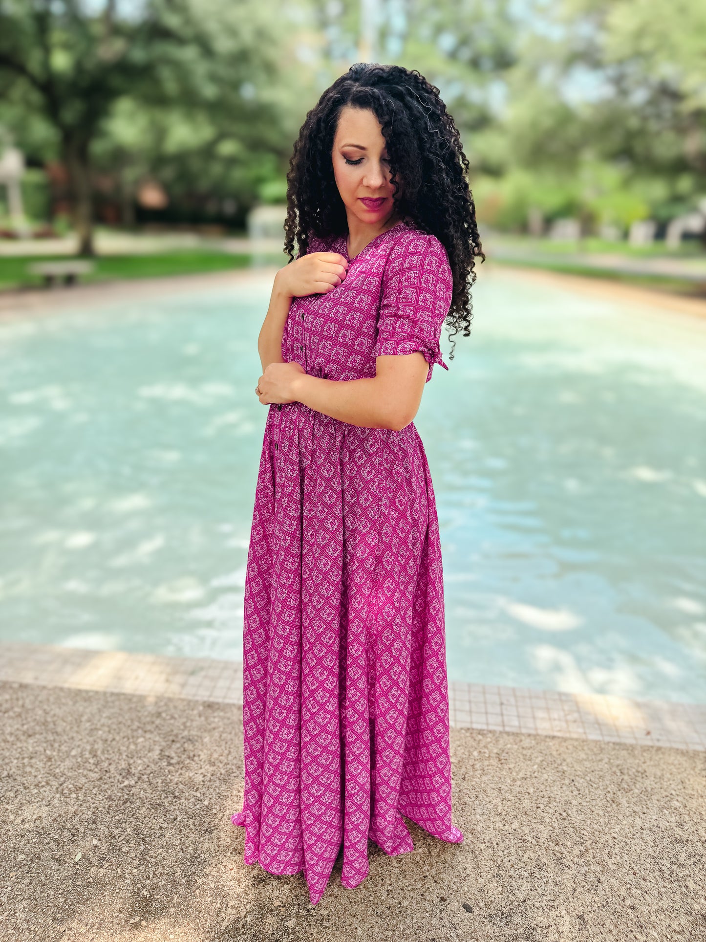 Woman in a pink modest nursing dress standing by a fountain in a park