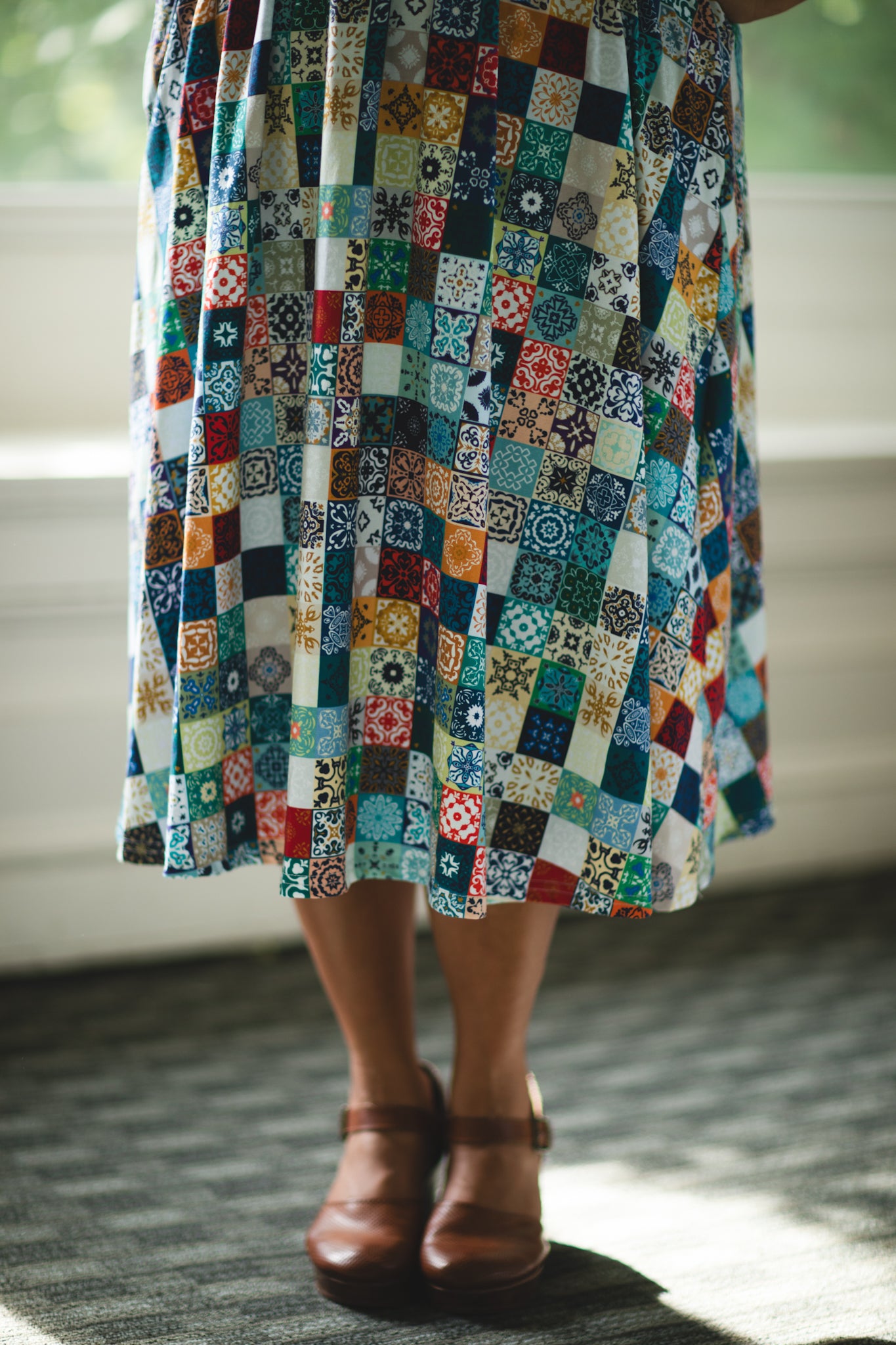 Person wearing a colorful patchwork modest nursing dress with a neutral background