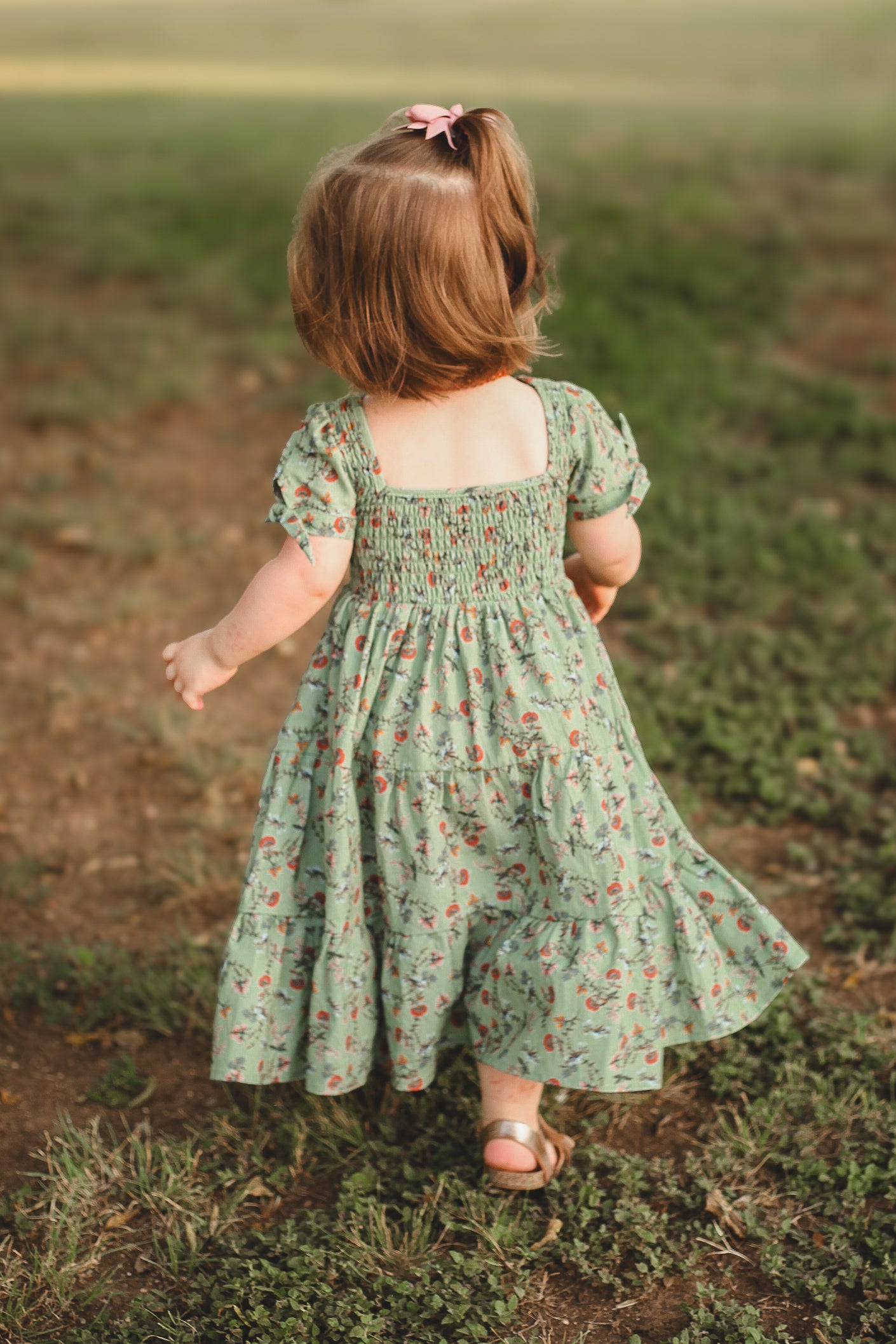 Child in a green floral dress standing in a field