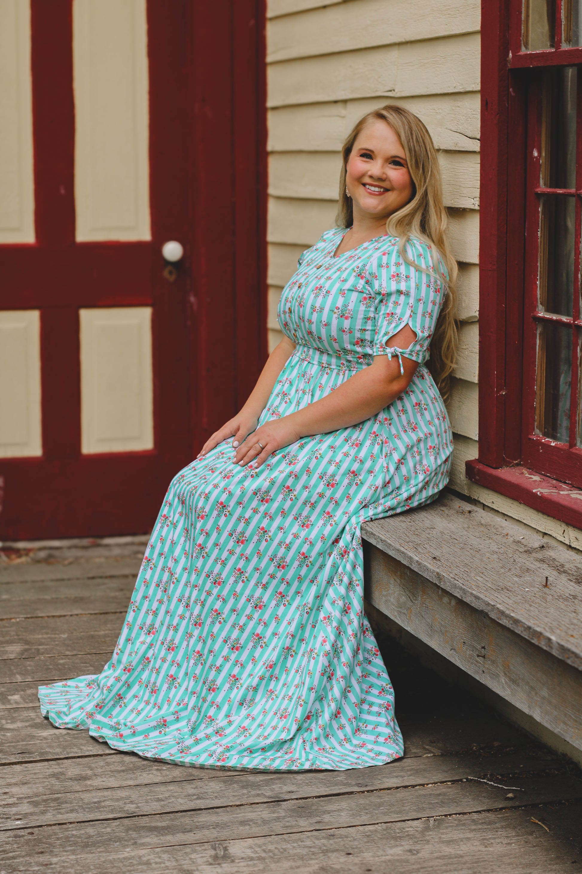 Woman in a turquoise modest dress sitting on a wooden porch.