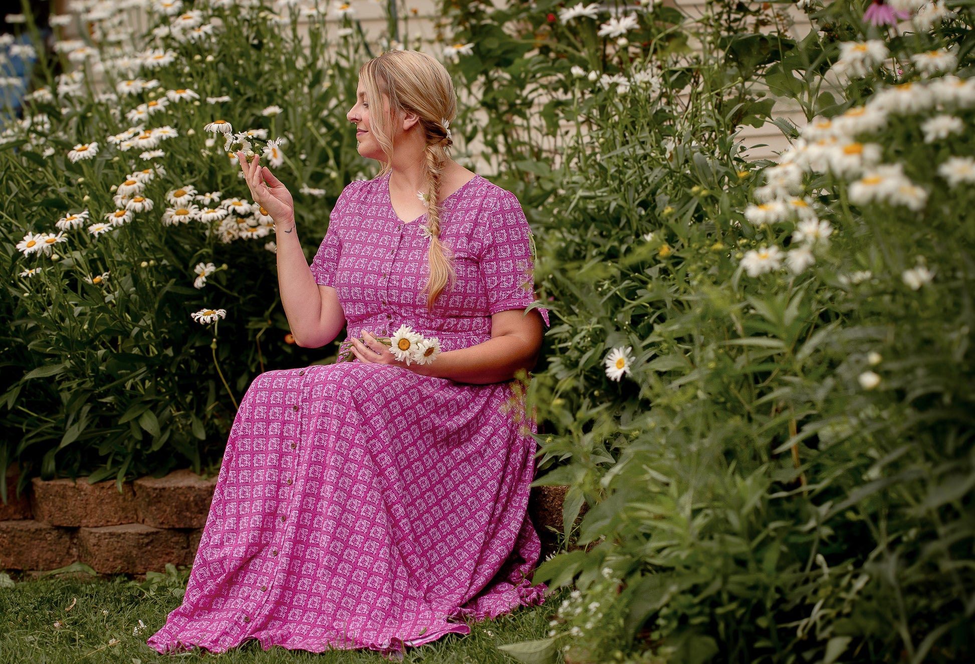 Woman in a pink modest nursing dress sitting among flowers in a garden