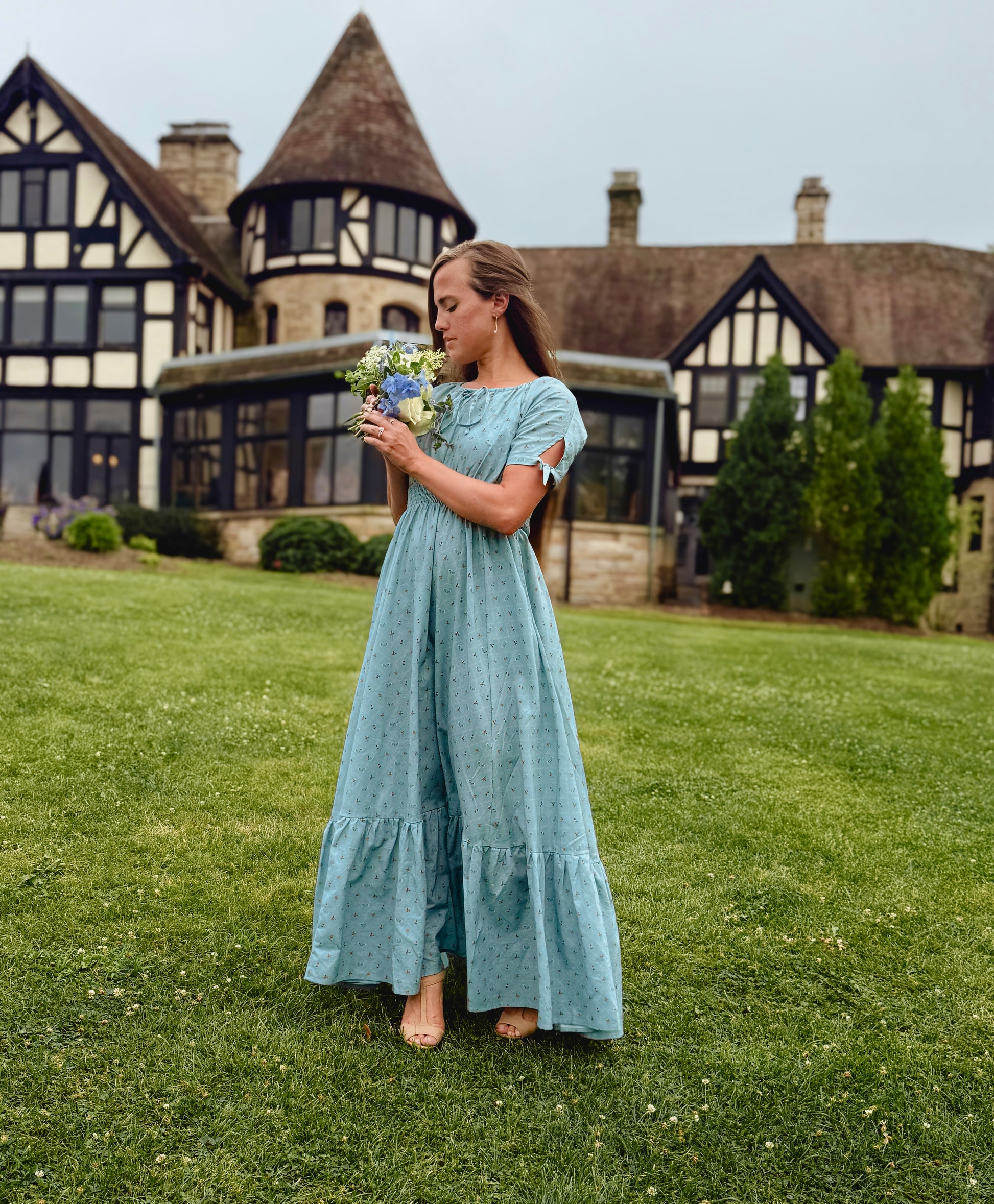 Woman in a light blue modest nursing dress holding flowers in front of a historic building