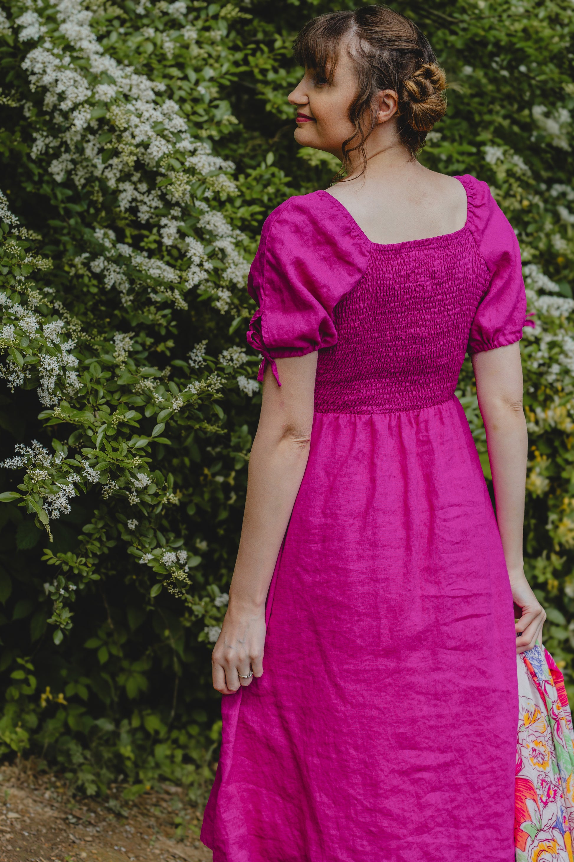 Woman wearing a bright pink modest nursing dress standing in front of green foliage.