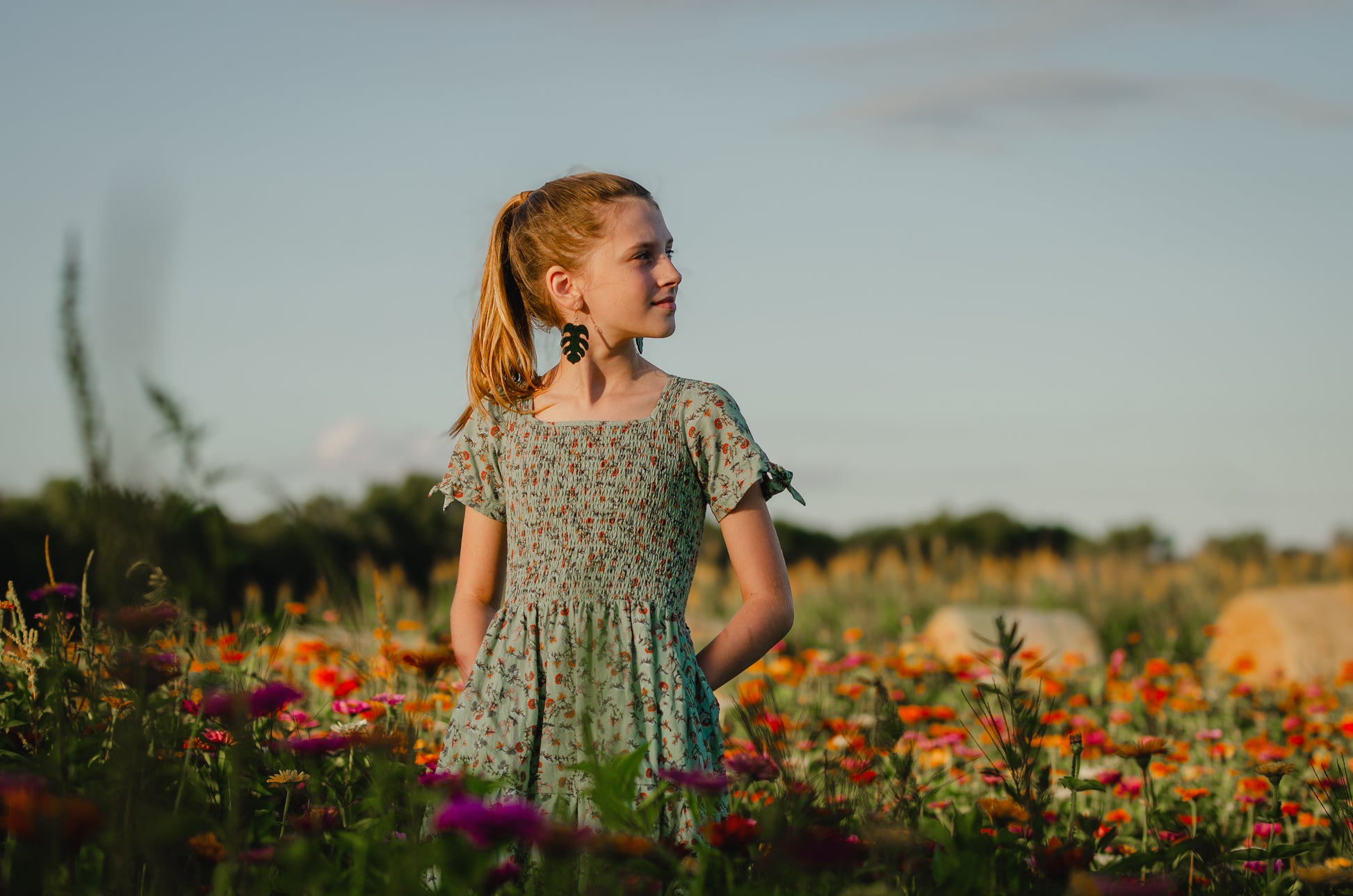 Young girl in a floral dress standing in a field of flowers with a blurred background