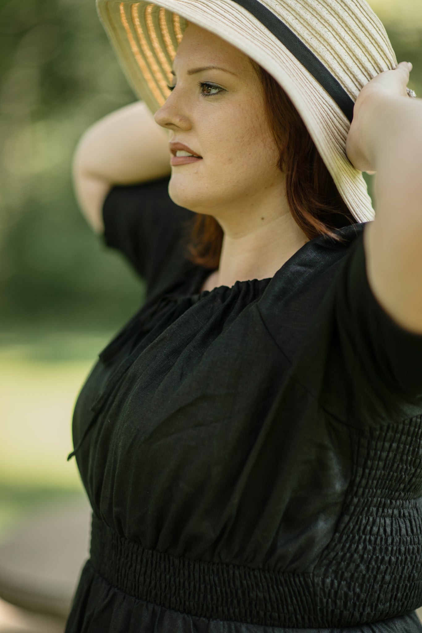 Woman wearing a black modest nursing dress and straw hat outdoors