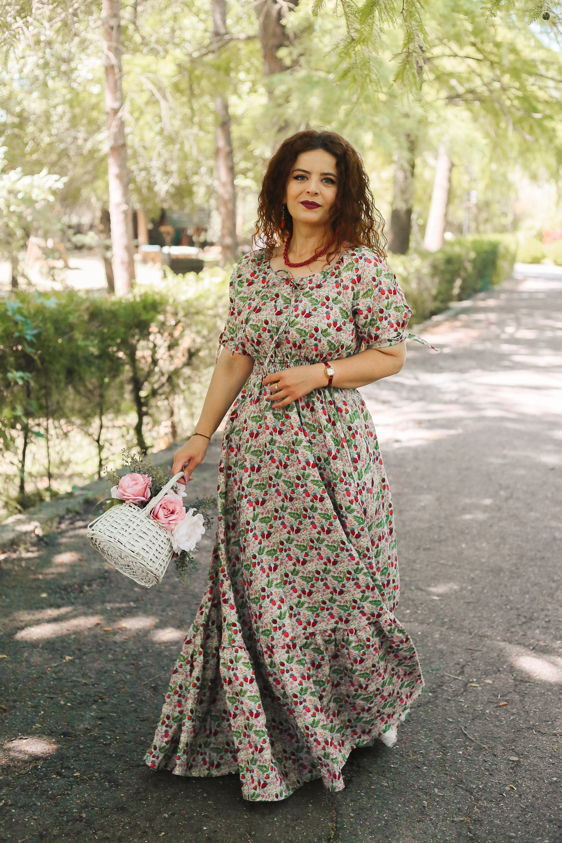 Woman in a floral modest nursing dress holding a bouquet of flowers outdoors.