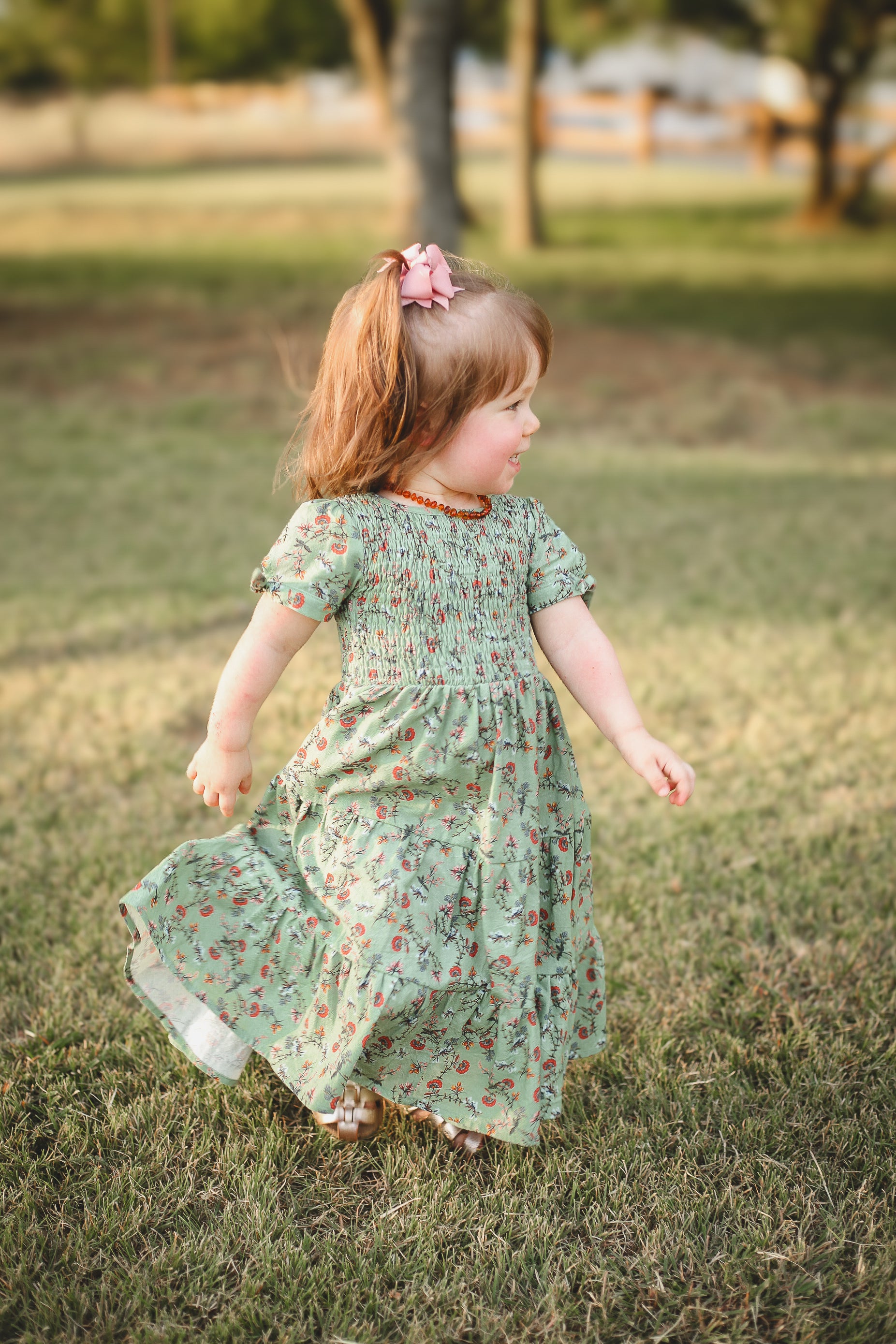 Young girl in a green floral dress running on grass with trees in the background