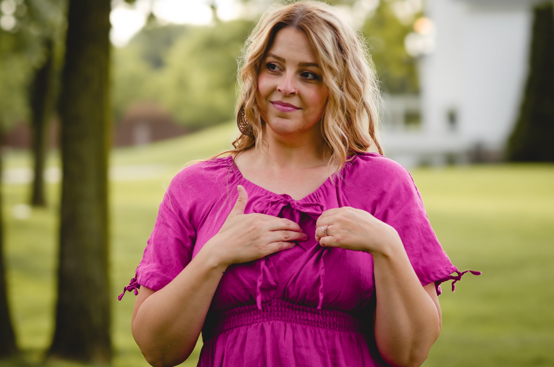 Woman in a pink modest nursing dress standing outdoors with trees and grass in the background
