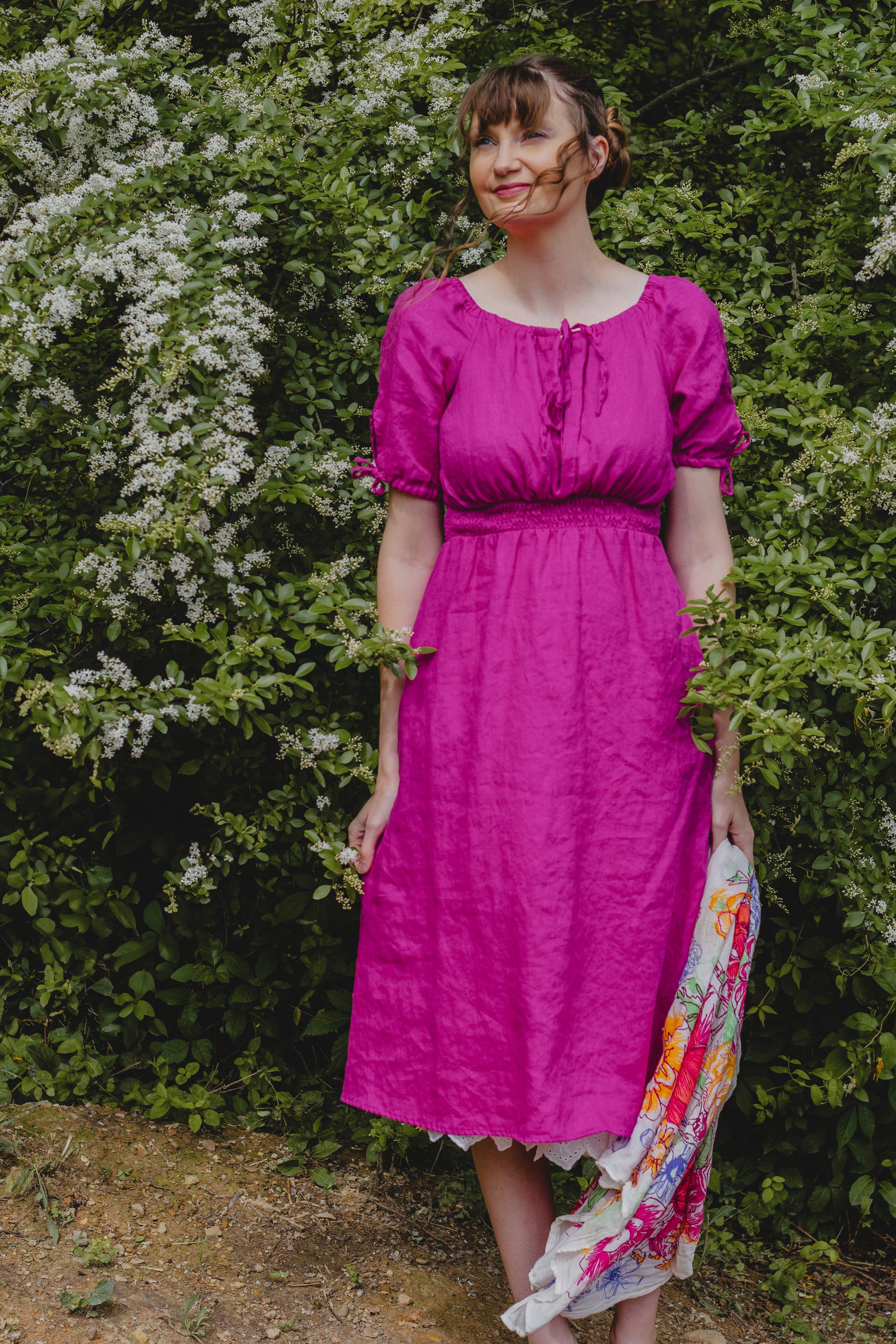 Woman in a bright pink modest nursing dress standing in front of green foliage