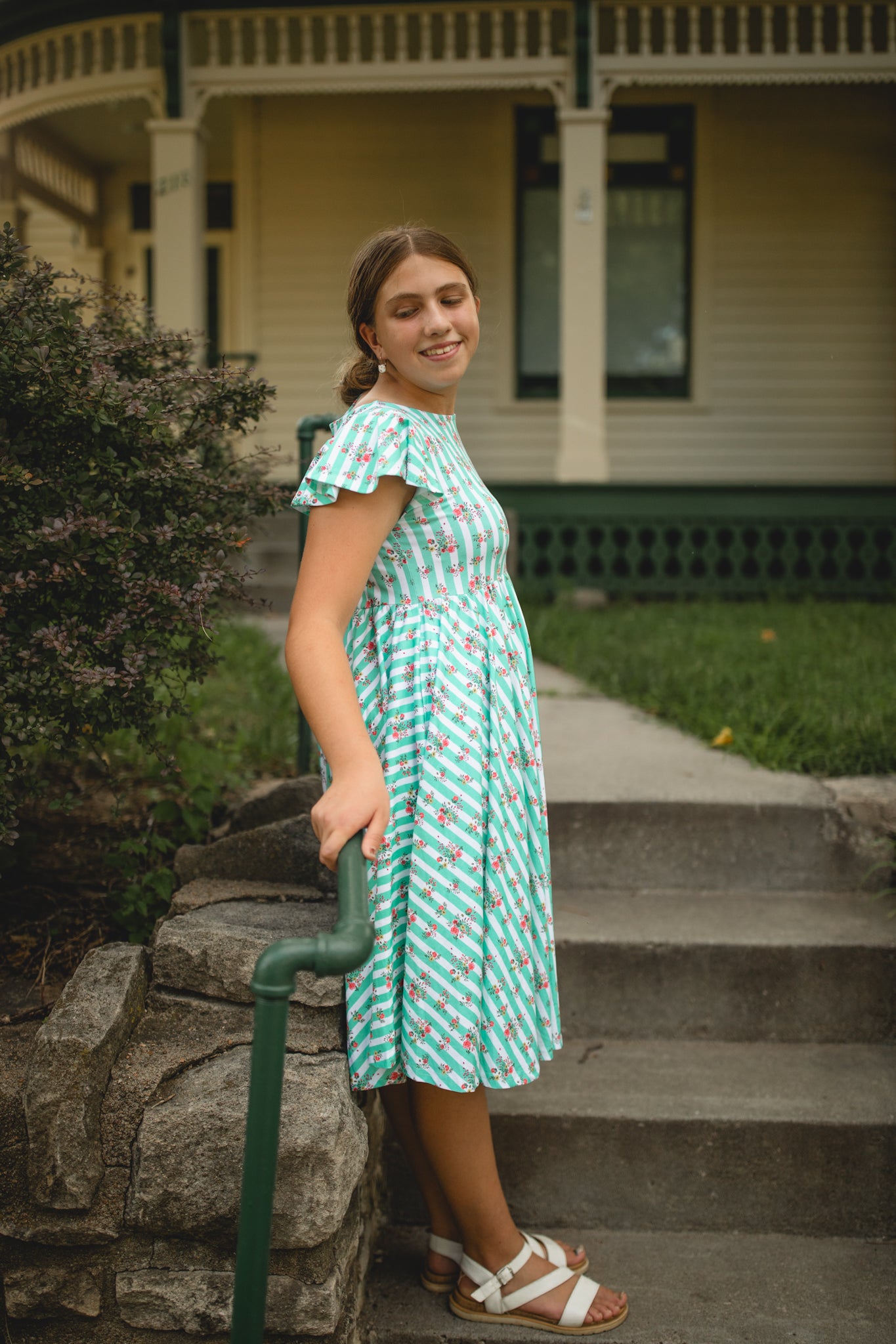 Woman in a green modest dress standing on steps outside a house