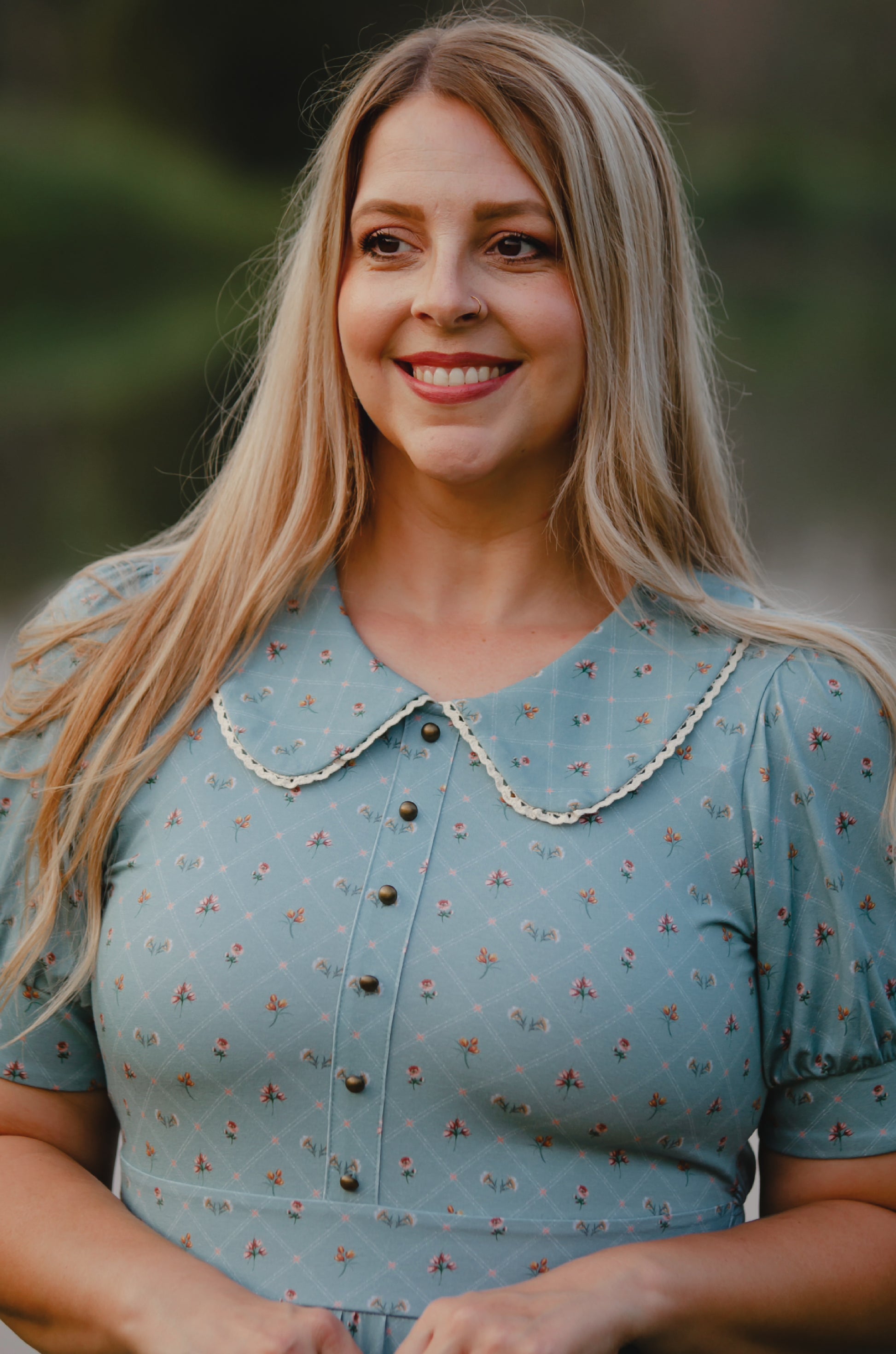 Woman wearing a blue modest nursing dress with a patterned collar against a blurred natural background