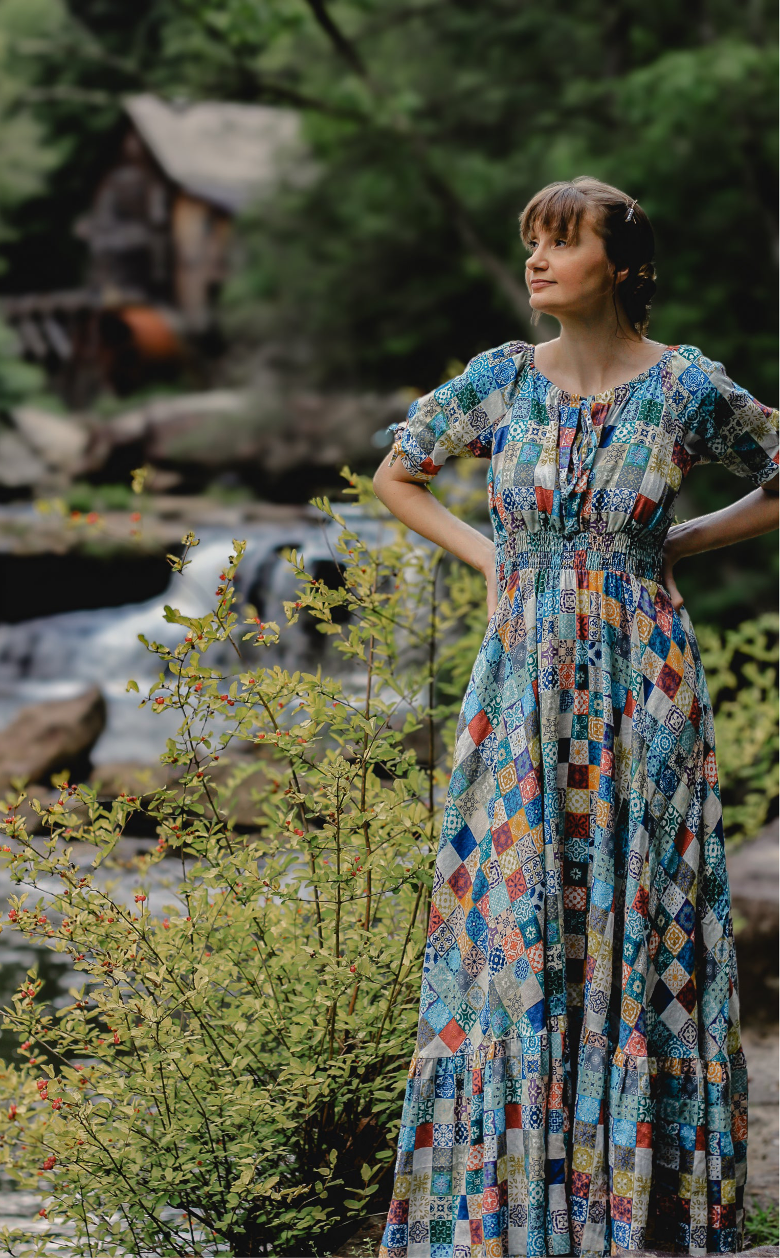 Woman in a colorful modest nursing dress standing by a stream with greenery in the background