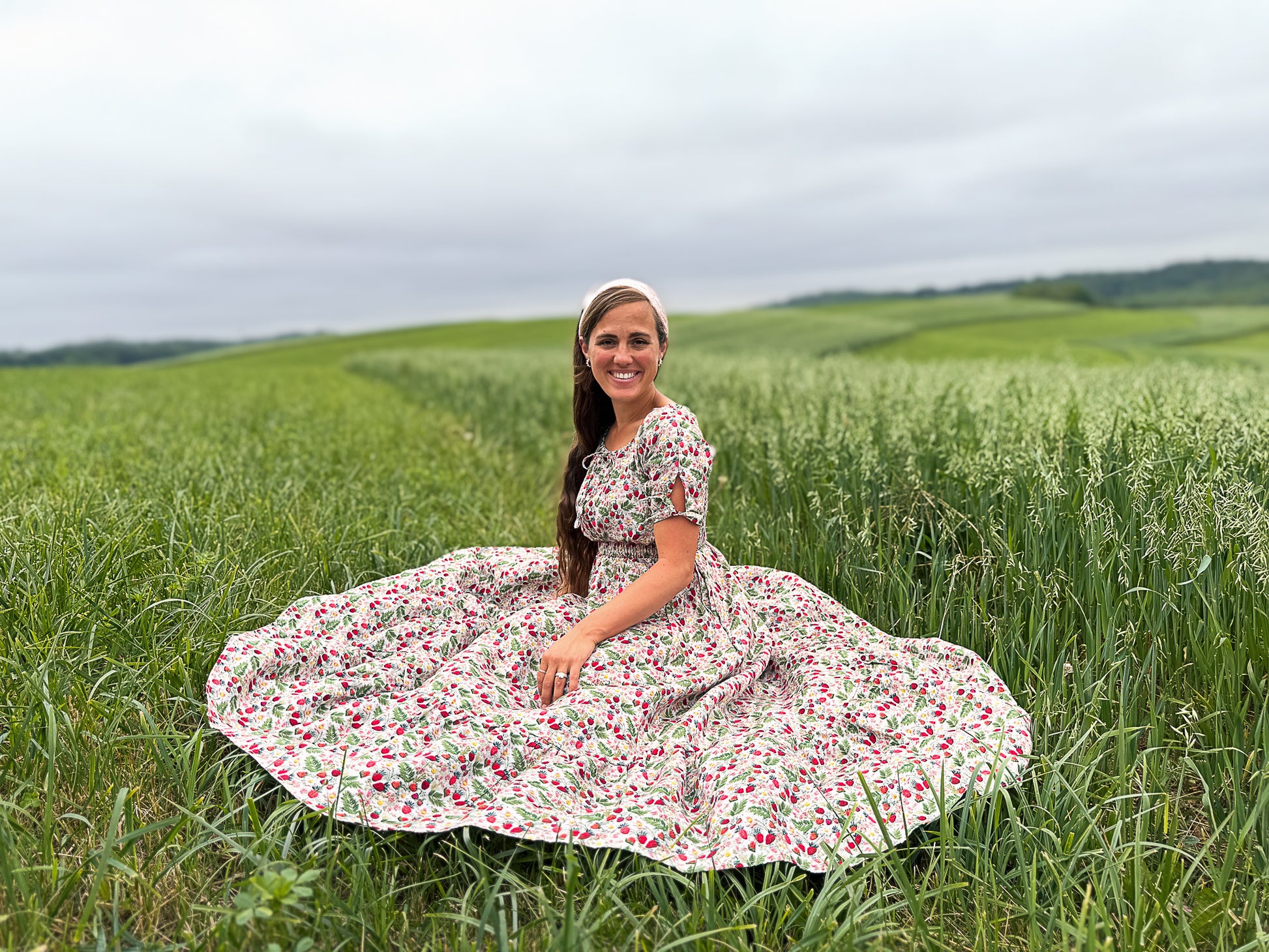 Woman in a floral modest nursing dress sitting in a green field