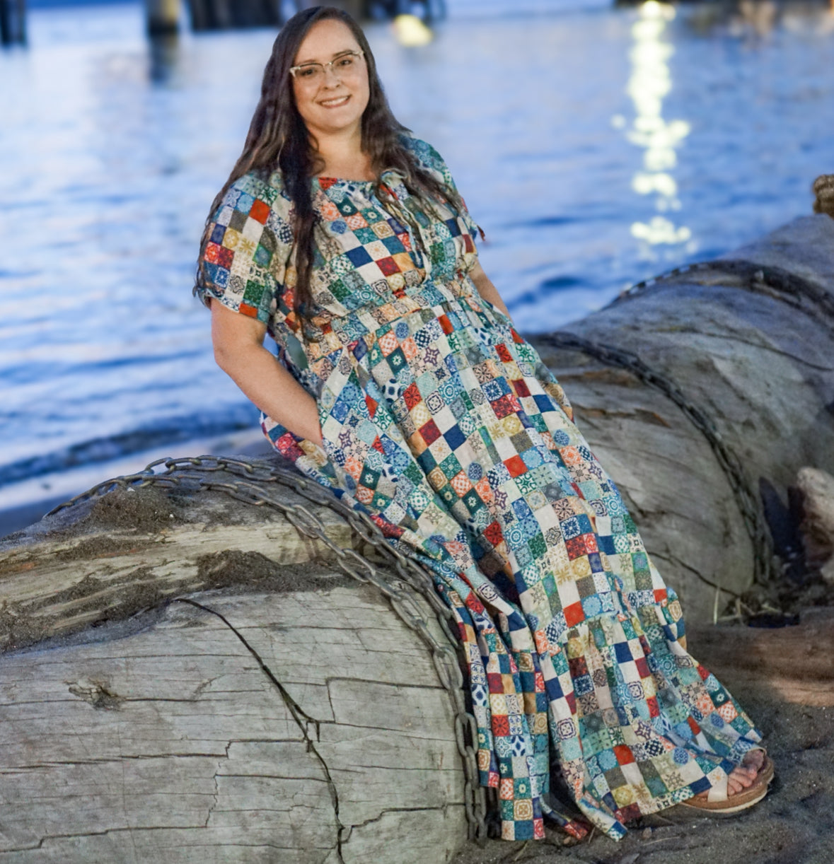 Woman in a colorful modest nursing dress sitting on a log by a body of water