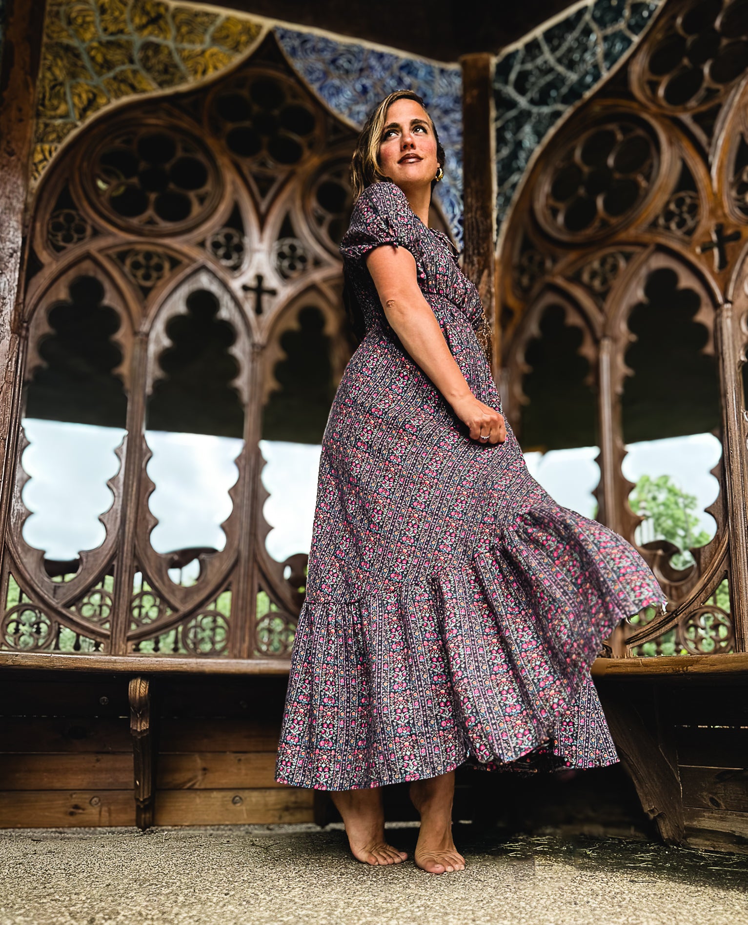 Woman in a floral modest nursing dress standing in front of ornate wooden arches.