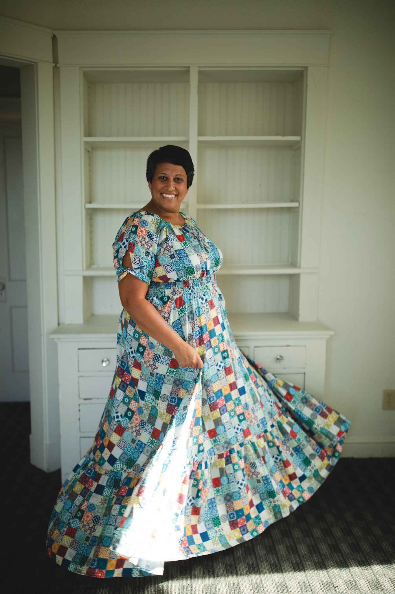 Woman in a colorful modest nursing dress standing in a room with white shelves.