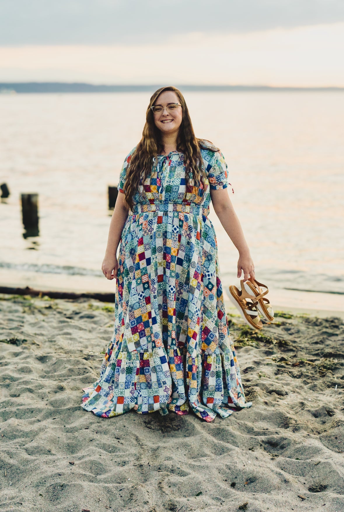 Woman in a colorful modest nursing dress standing on a beach with water in the background