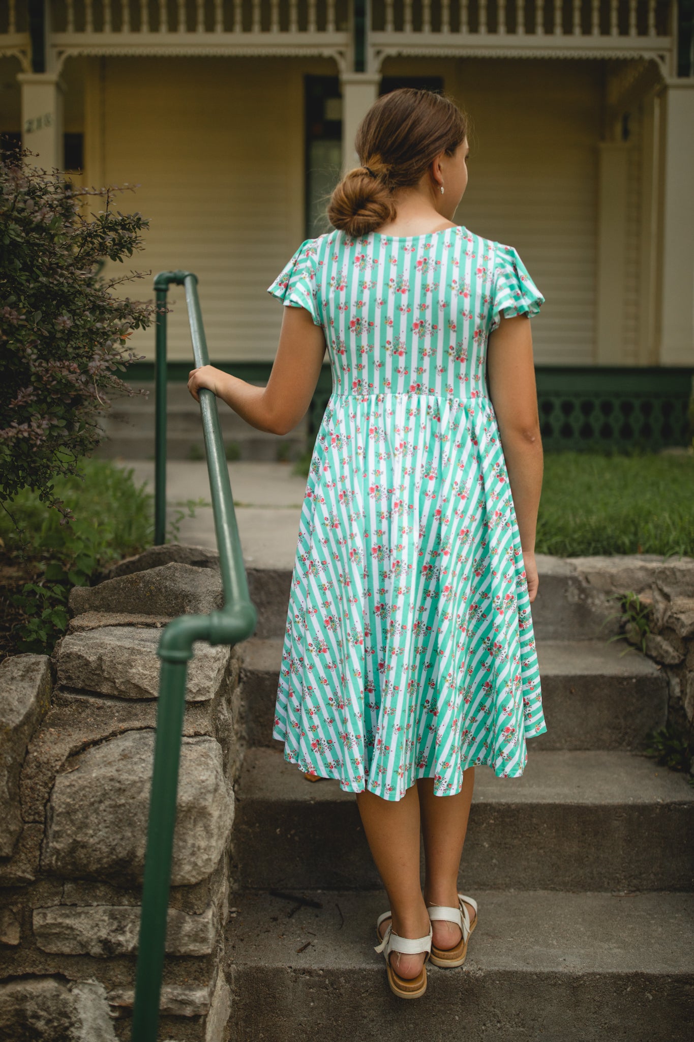 Woman in a green patterned modest dress walking up steps outdoors.