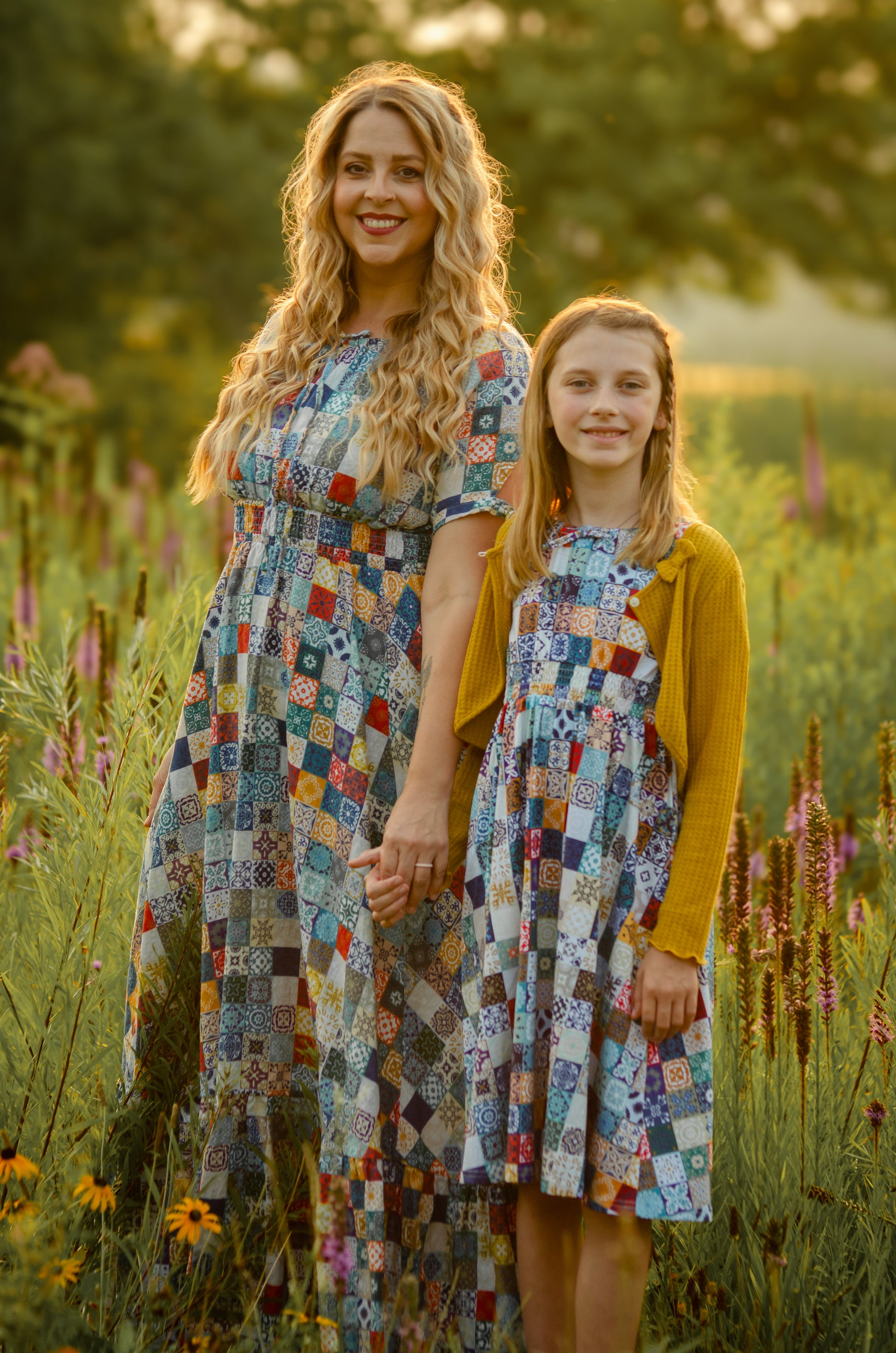 Woman and young girl in matching floral modest dresses standing in a field of flowers.