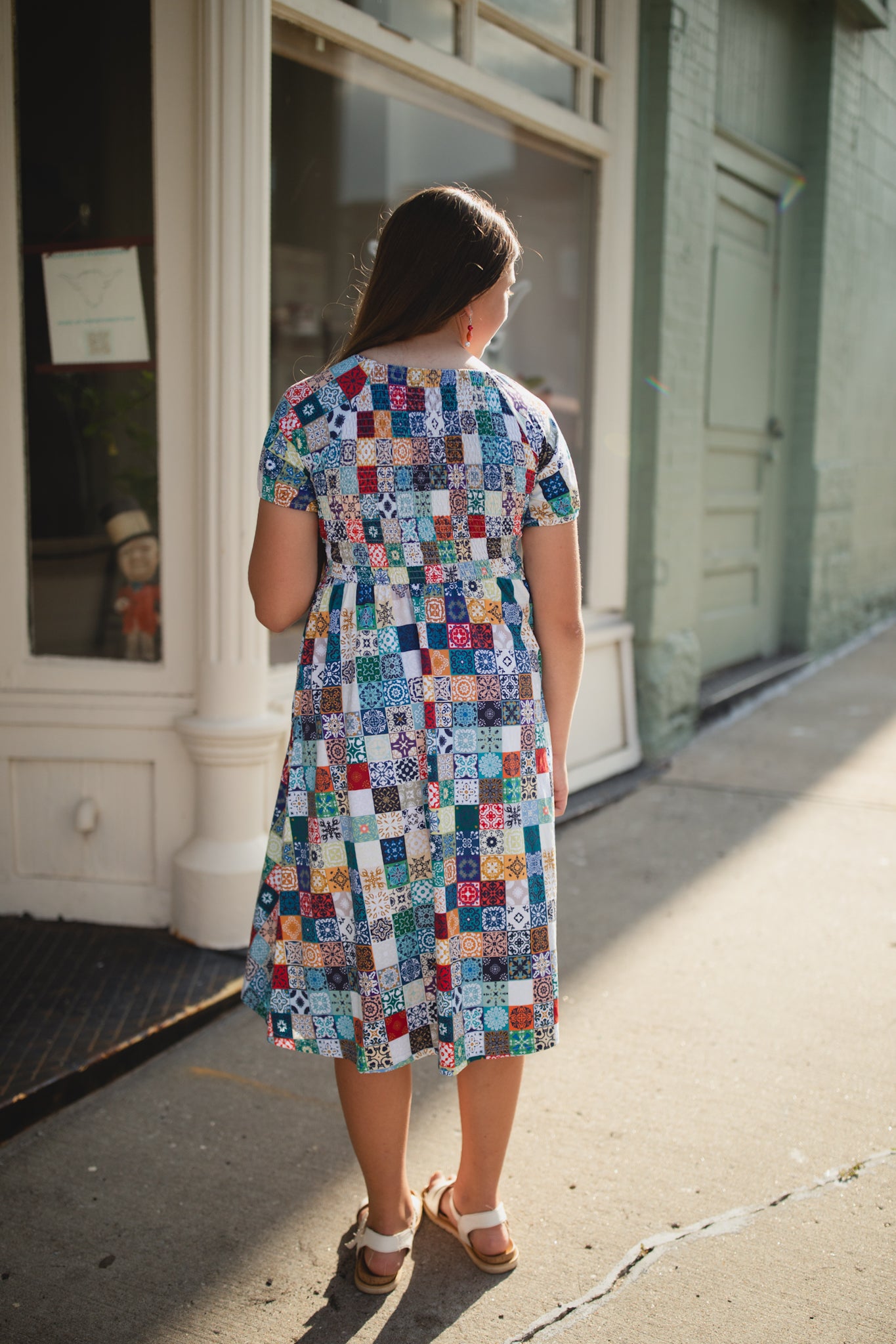 Woman wearing a colorful patchwork modest nursing dress standing on a sidewalk.