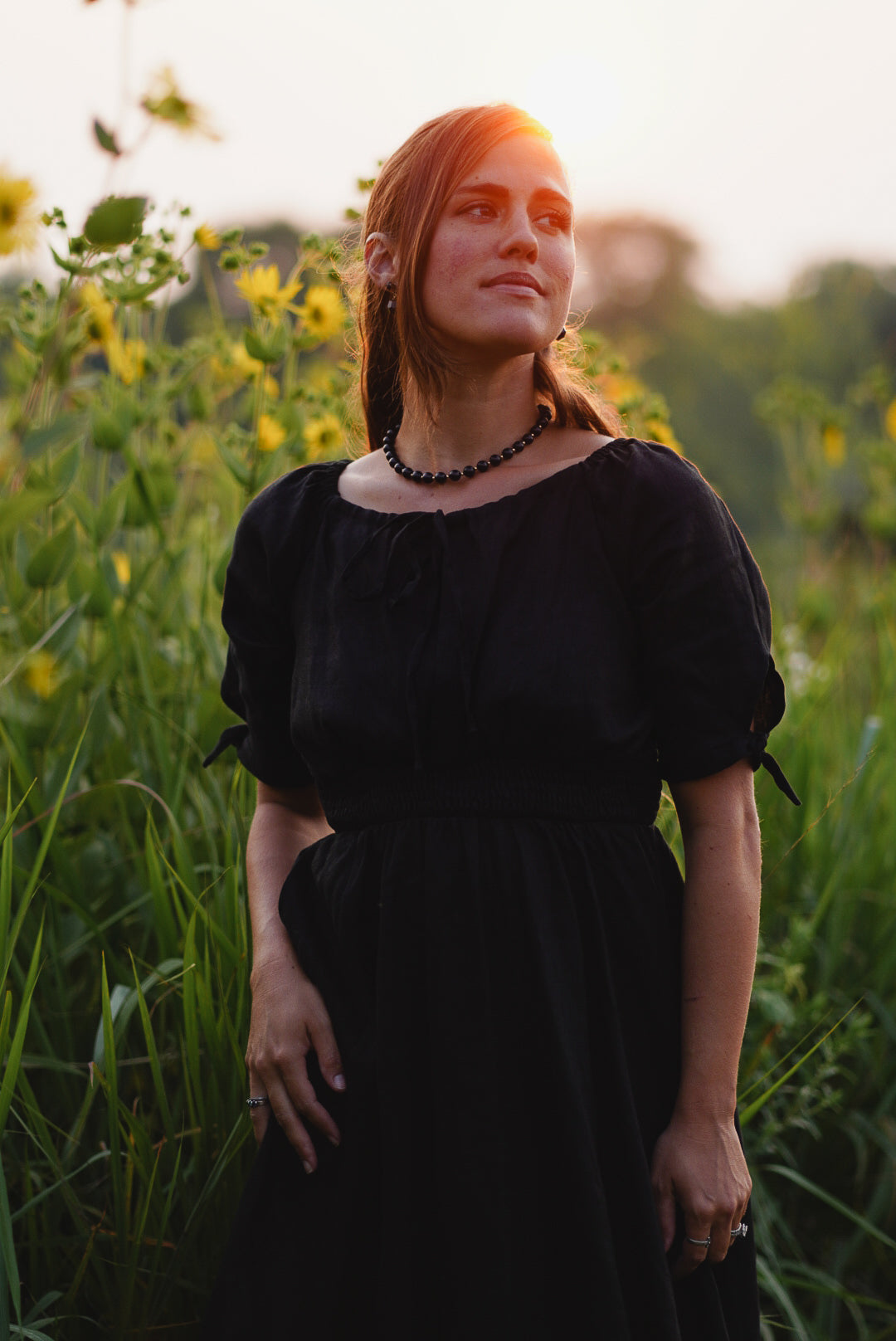 Woman in a black modest nursing dress standing in a sunflower field