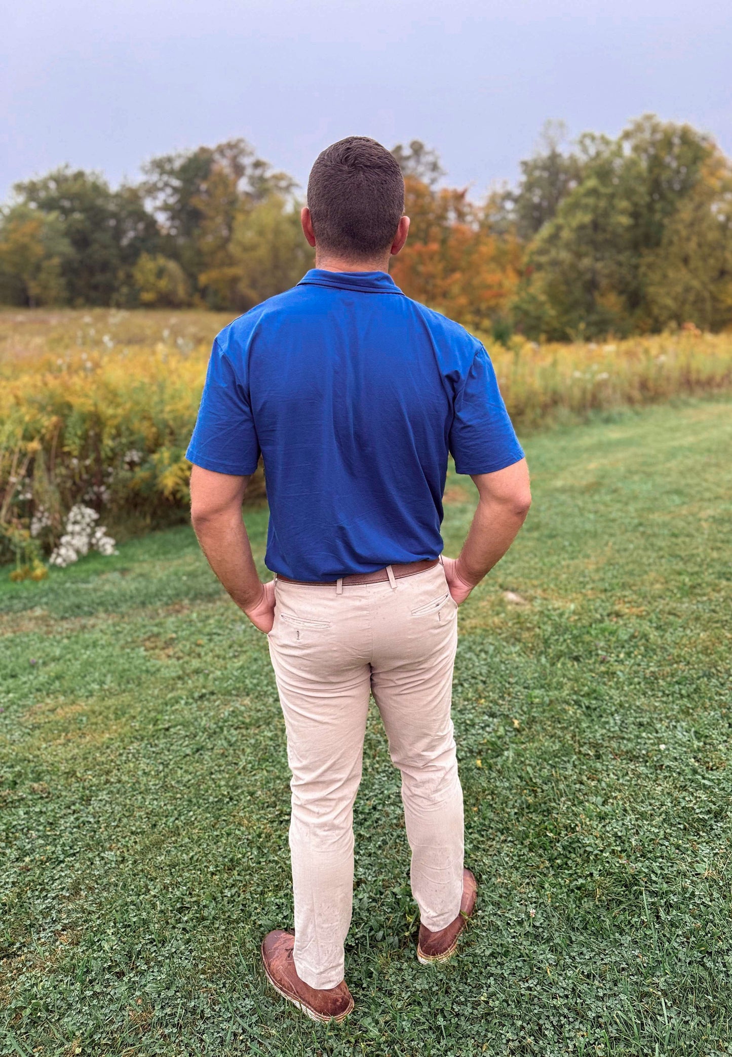 Man in blue polo in grassy field.