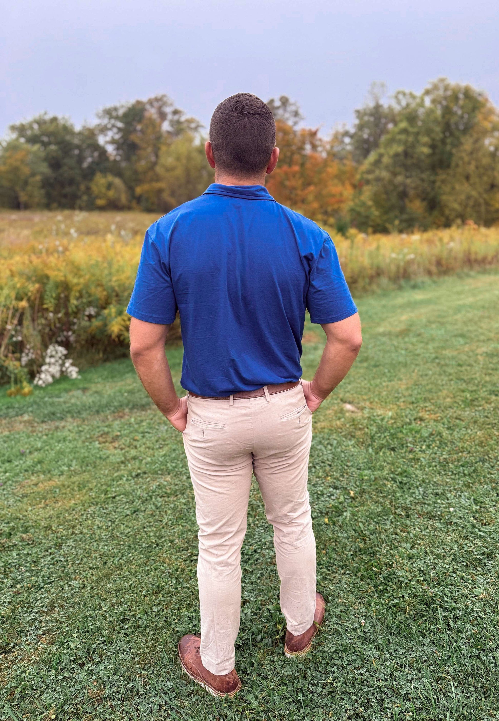 Man in blue polo in grassy field.