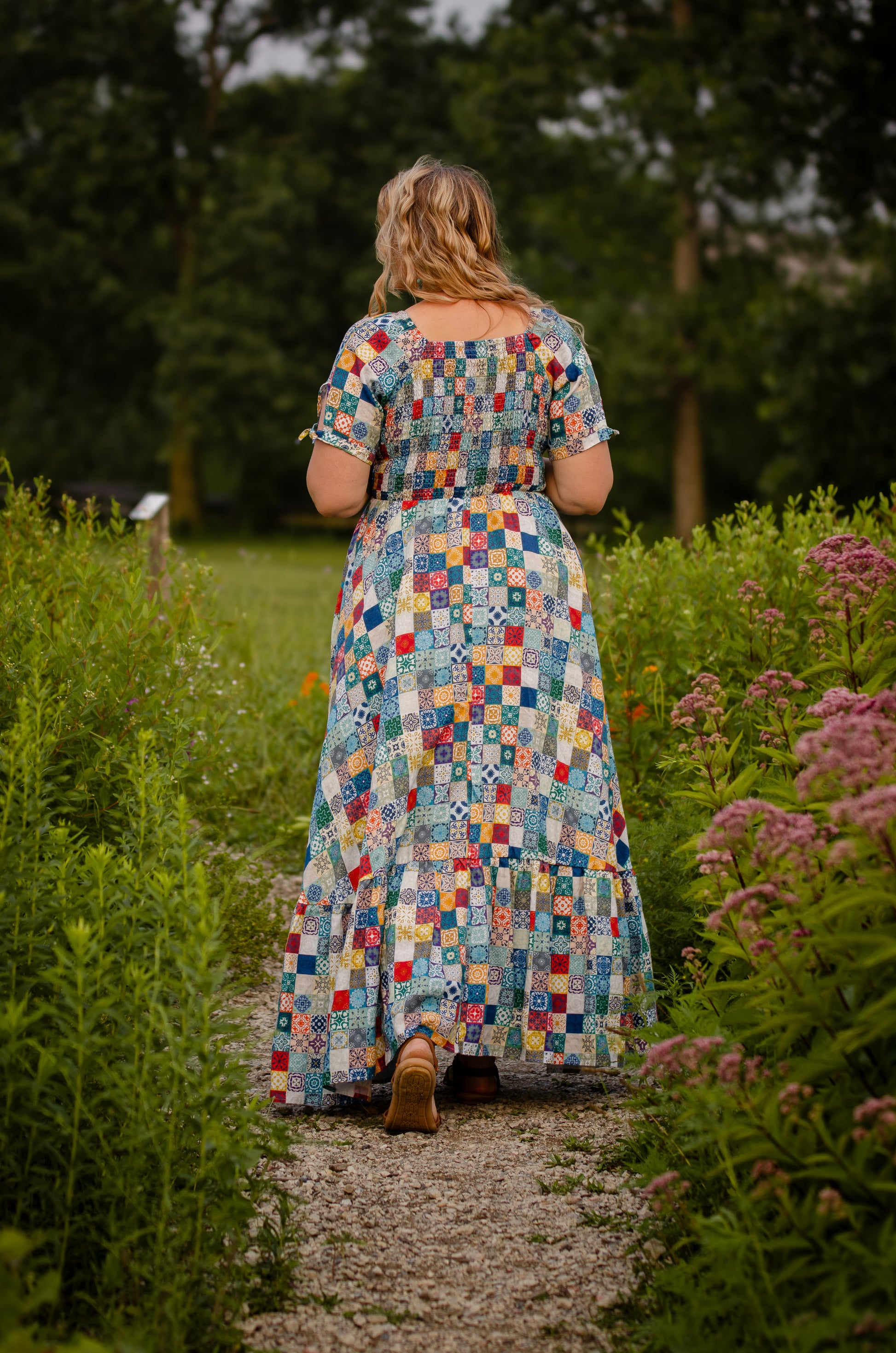 Woman in a colorful checkered modest nursing dress walking through a garden path.