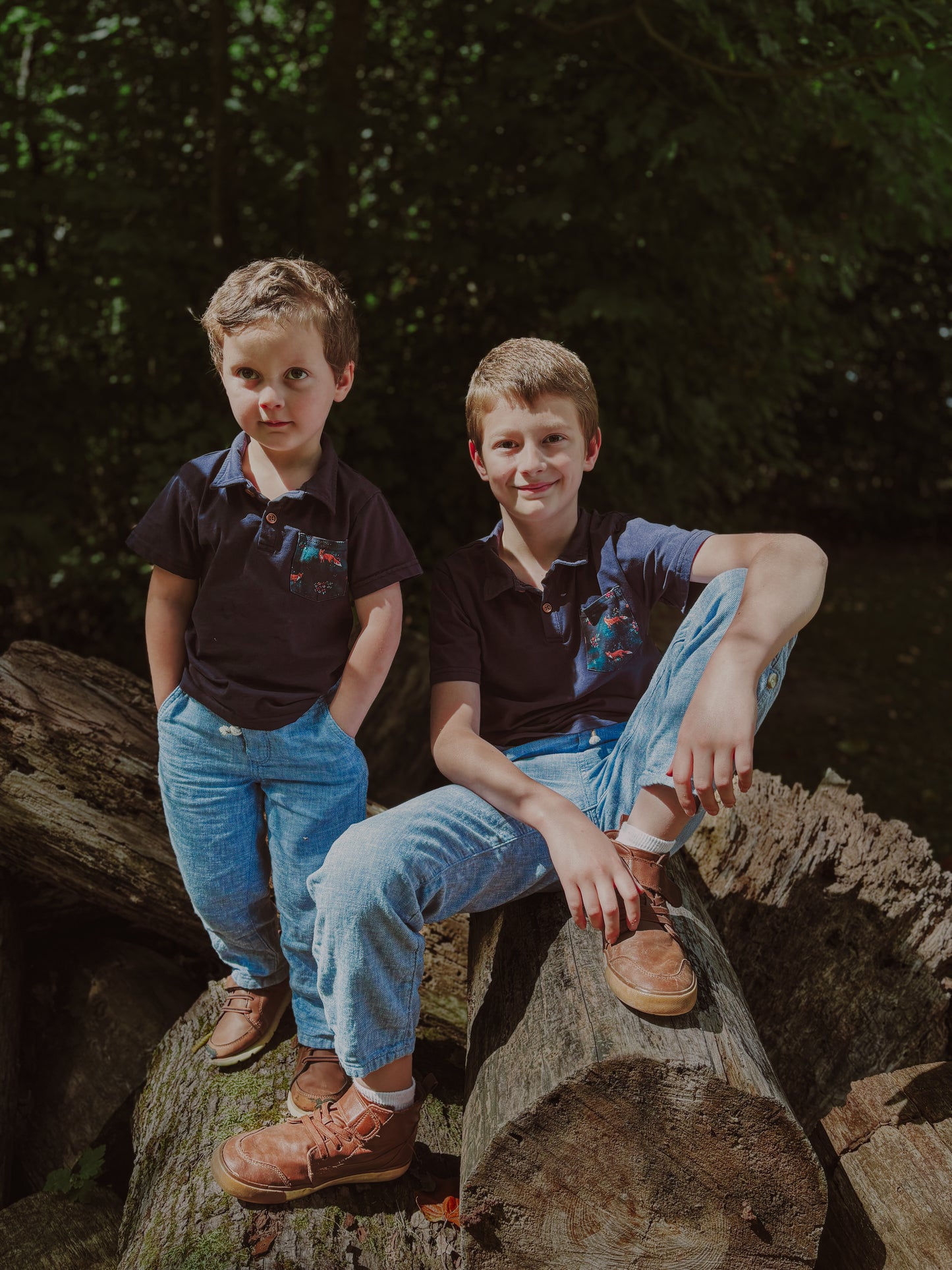 Two boys sitting on logs in forest.